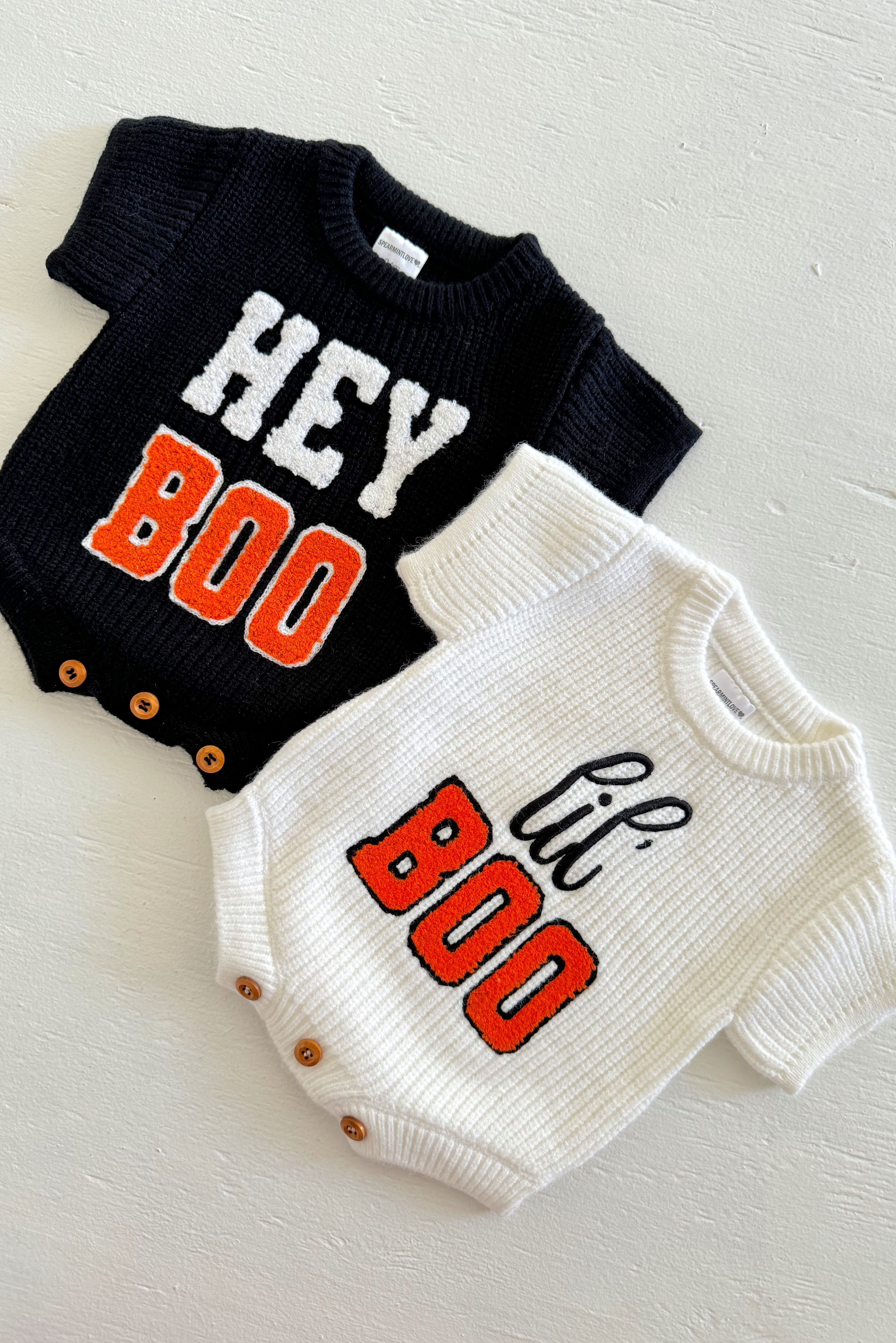 Black and white knitted baby bodysuits with "Hey Boo" and "lil' Boo" text in orange and black.