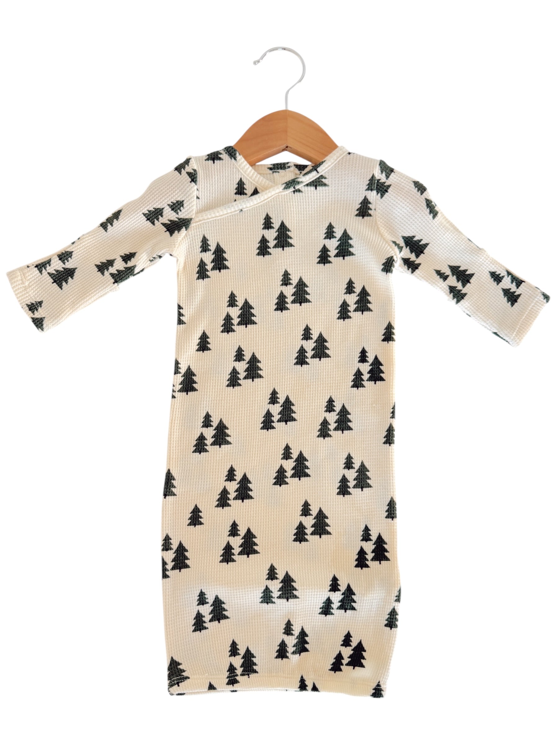 Long-sleeve baby outfit with a cream background and black tree patterns, hanging on a wooden hanger.