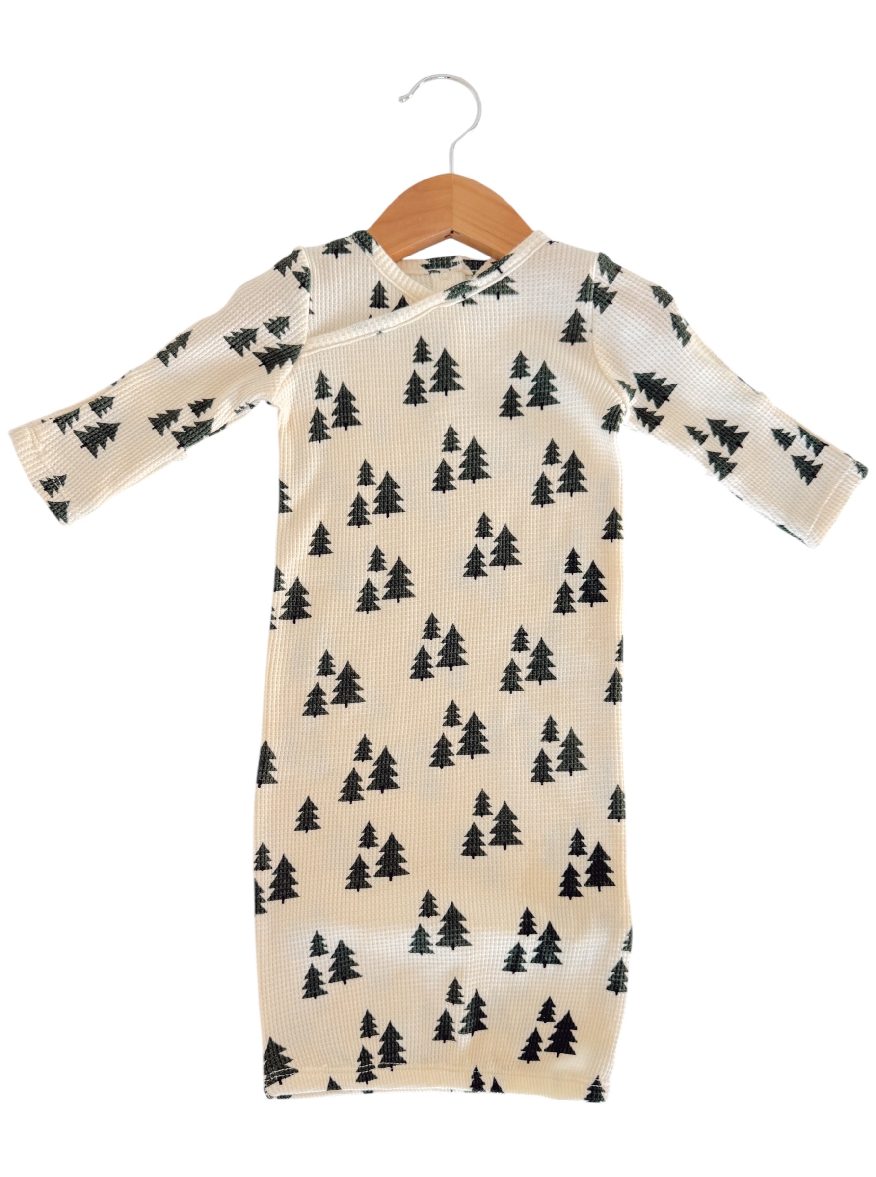 Long-sleeve baby outfit with a cream background and black tree patterns, hanging on a wooden hanger.