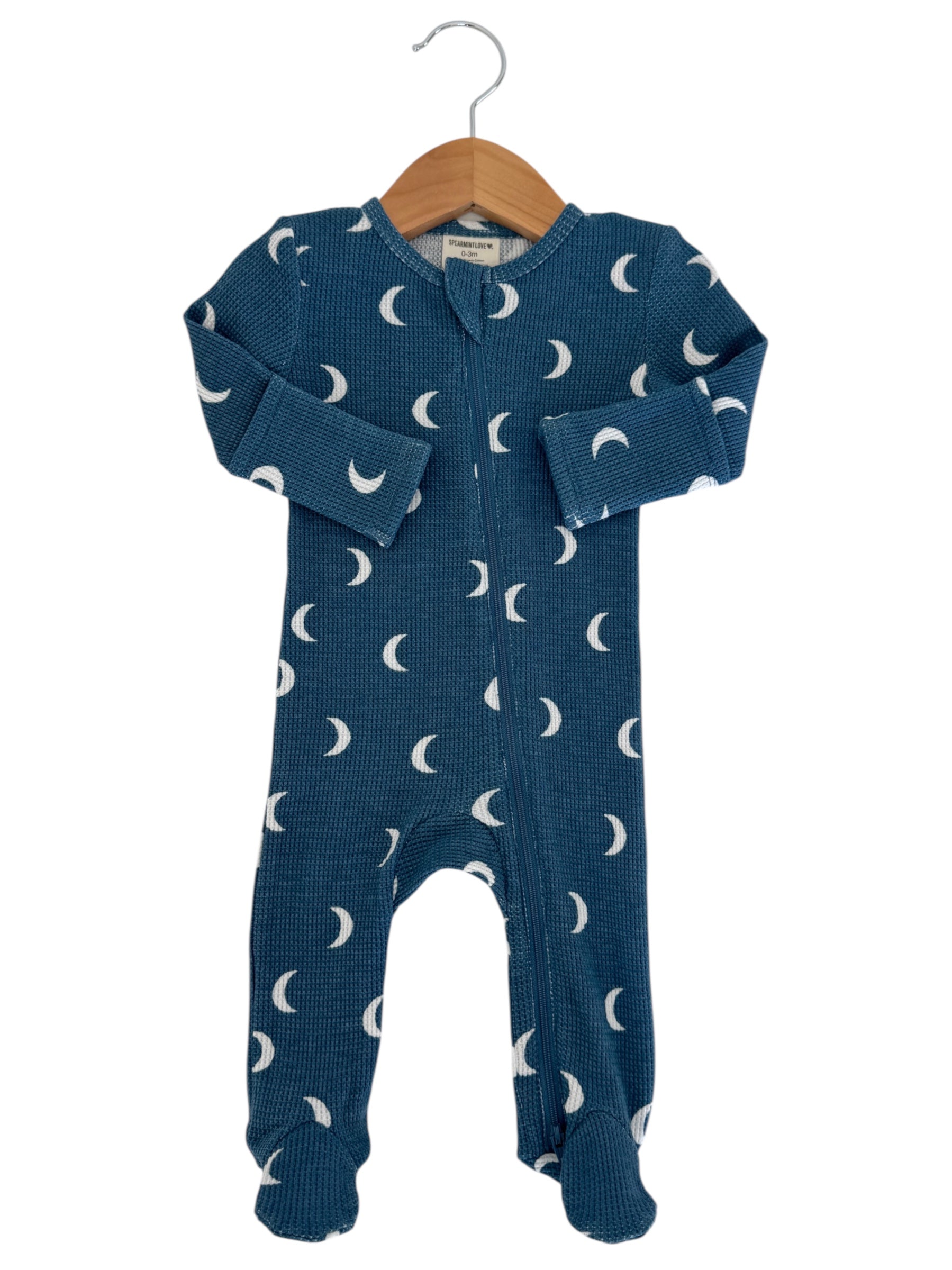 Blue baby onesie with white crescent moon patterns, hanging on a wooden hanger against a white background.