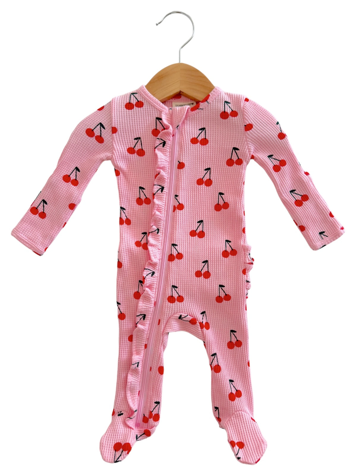 Pink baby onesie with cherry prints, featuring long sleeves and a zip closure, hung on a wooden hanger.