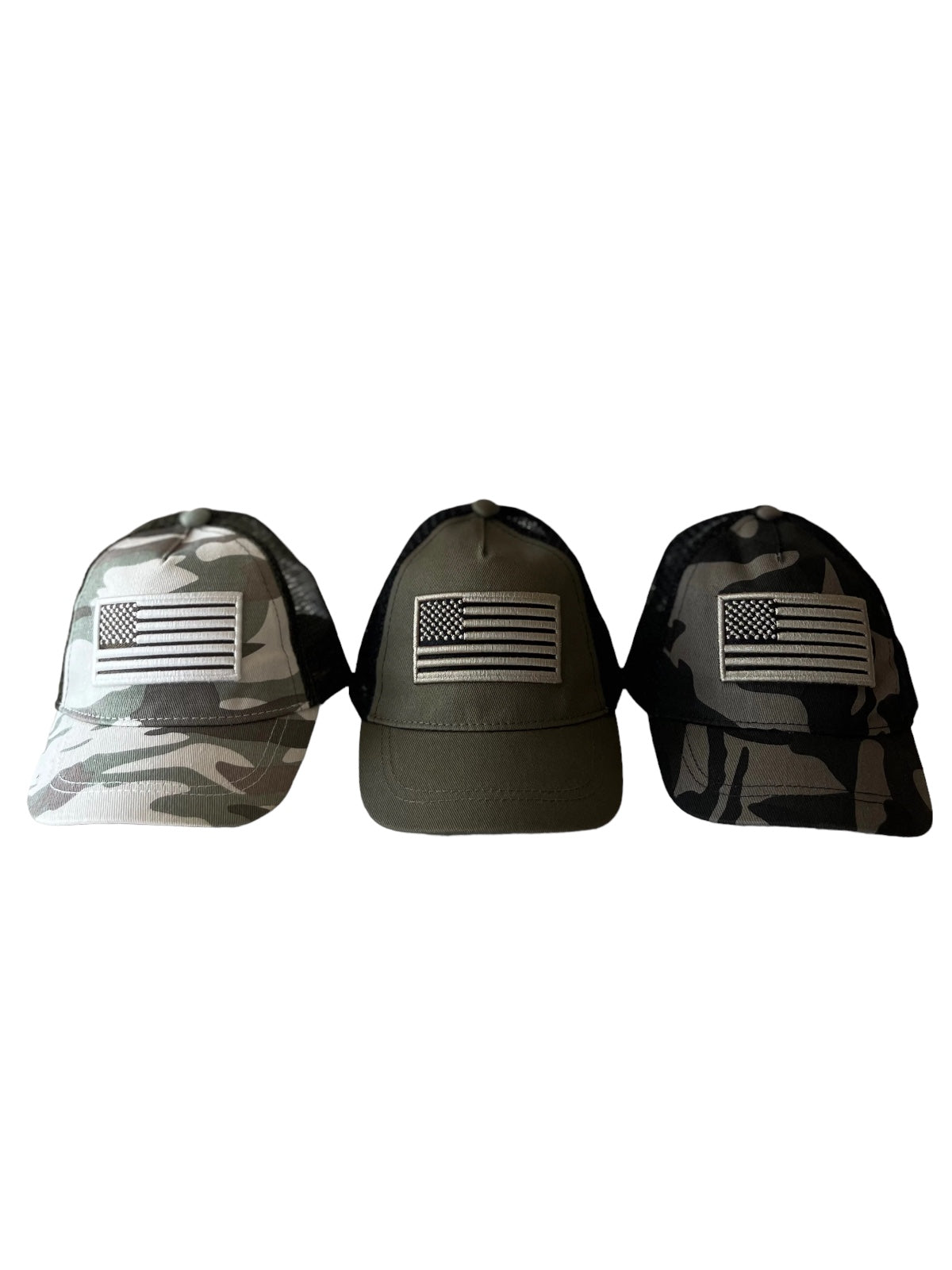 Three caps displaying American flags: one in camo, one in olive green, and one in black camo.