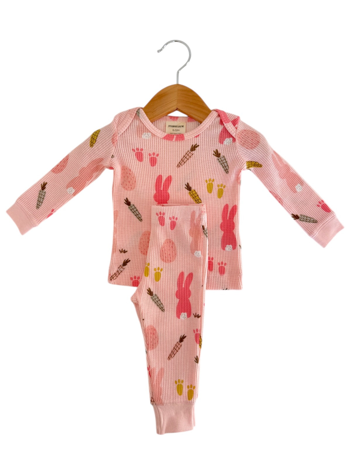 Pink children's pajama set with bunny and fruit patterns hanging on a wooden hanger.