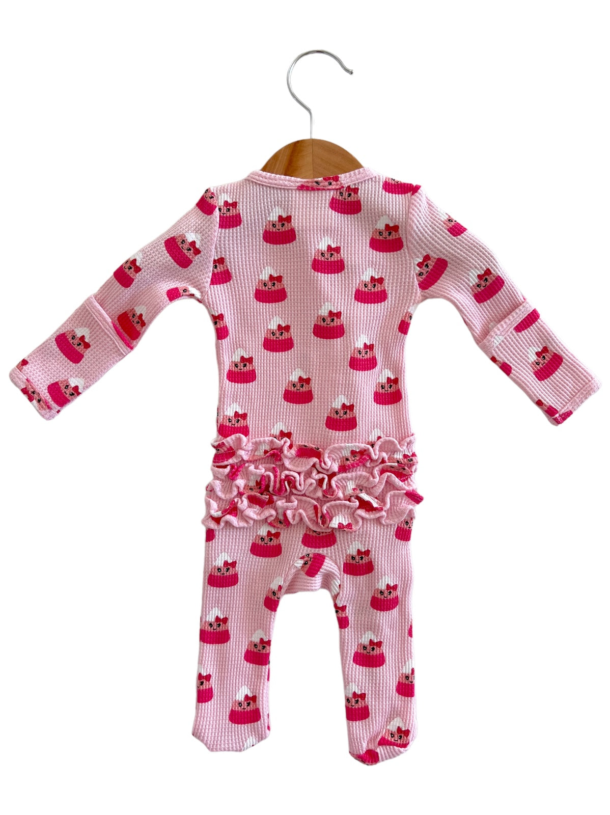 Pink baby onesie with cupcake pattern and ruffled trim, hanging on a wooden hanger.