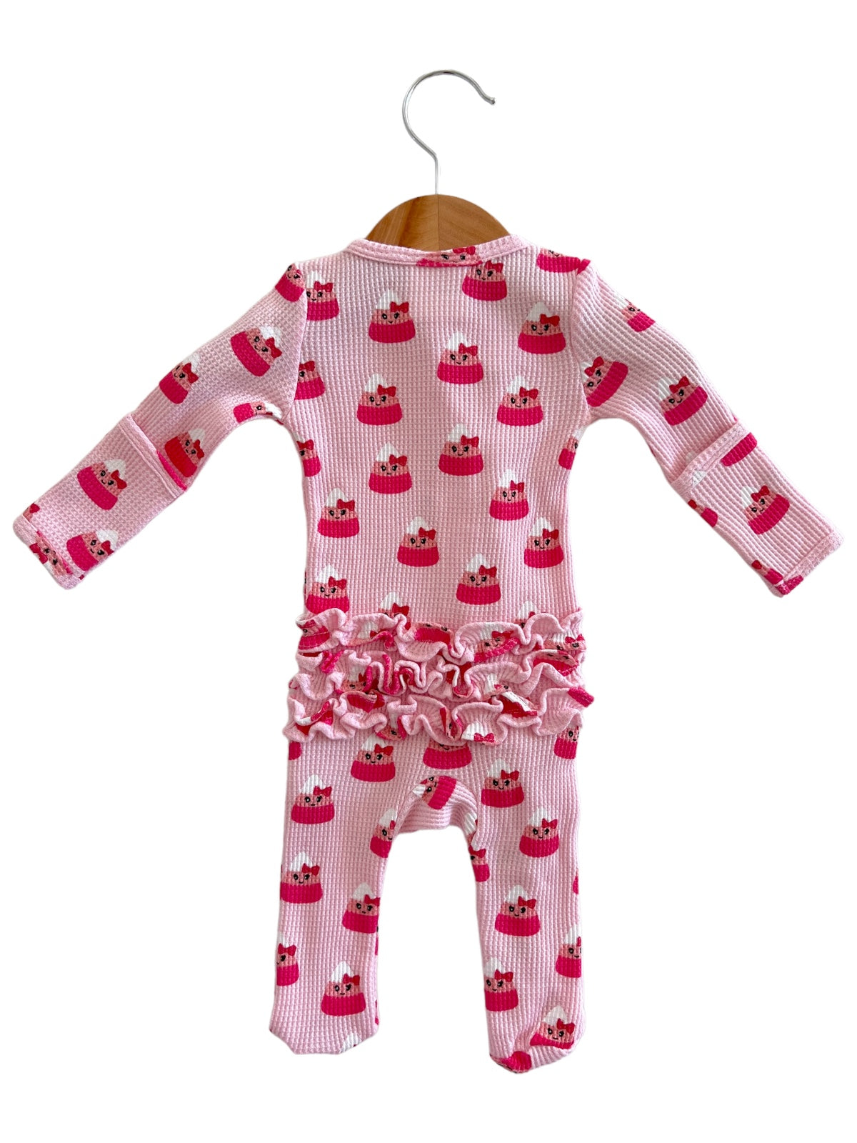Pink baby onesie with cupcake pattern and ruffled trim, hanging on a wooden hanger.