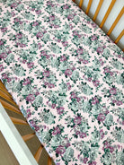 Floral-patterned crib sheet with pink background, featuring roses in green and purple hues.