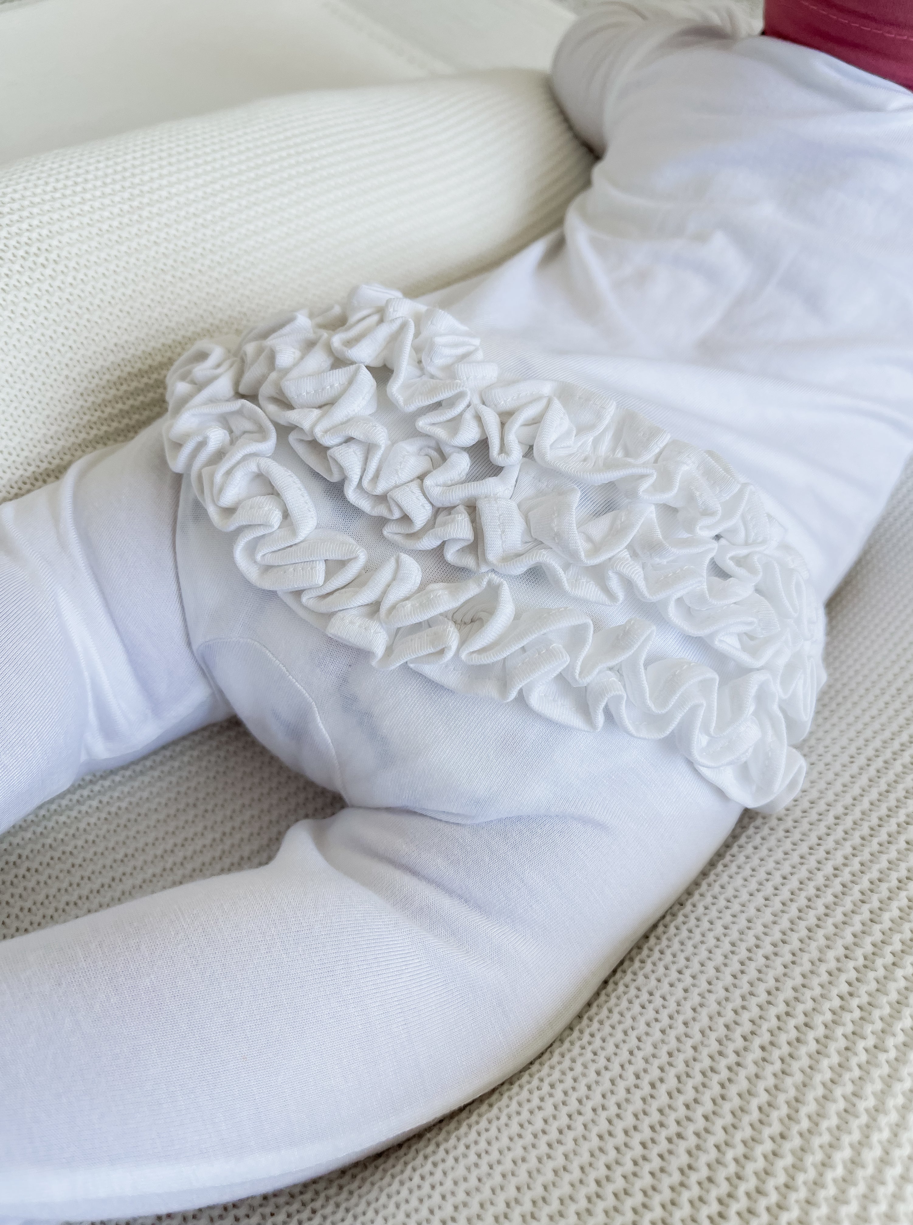 White onesie with ruffled details on the back, laid on a textured surface.