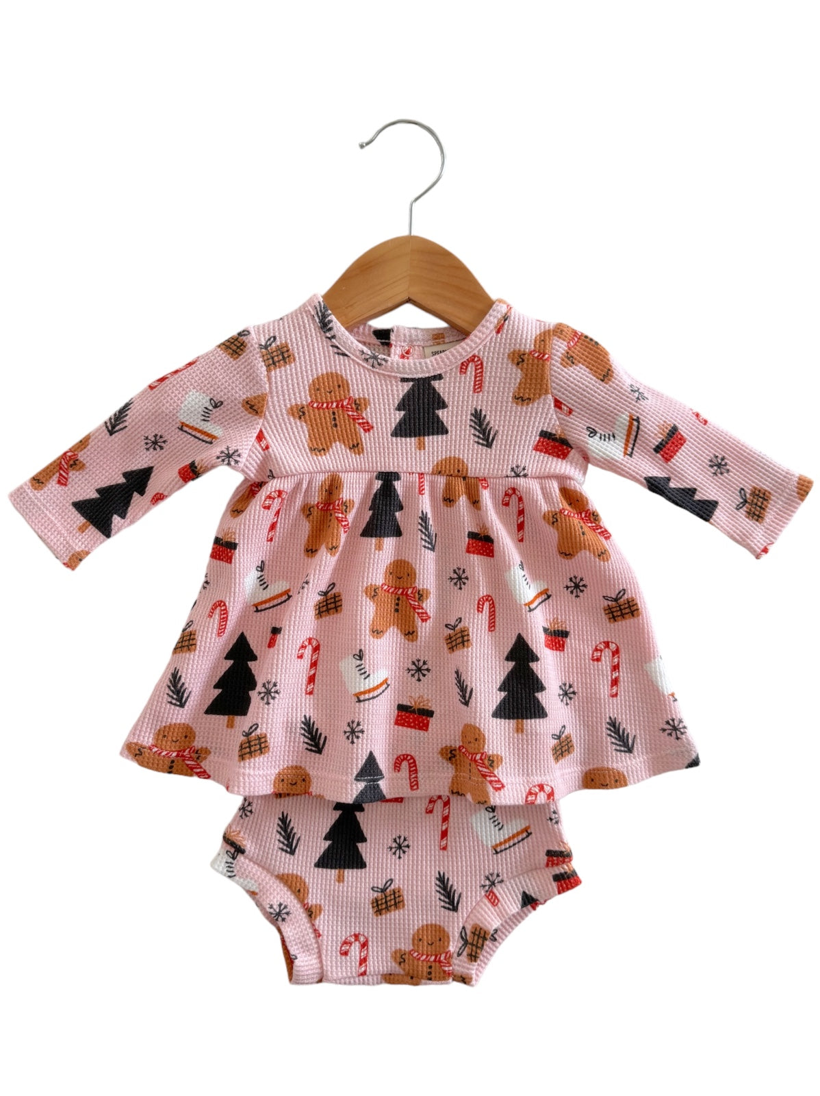 Pink toddler dress with gingerbread, candy canes, and Christmas trees, hanging on a wooden hanger.