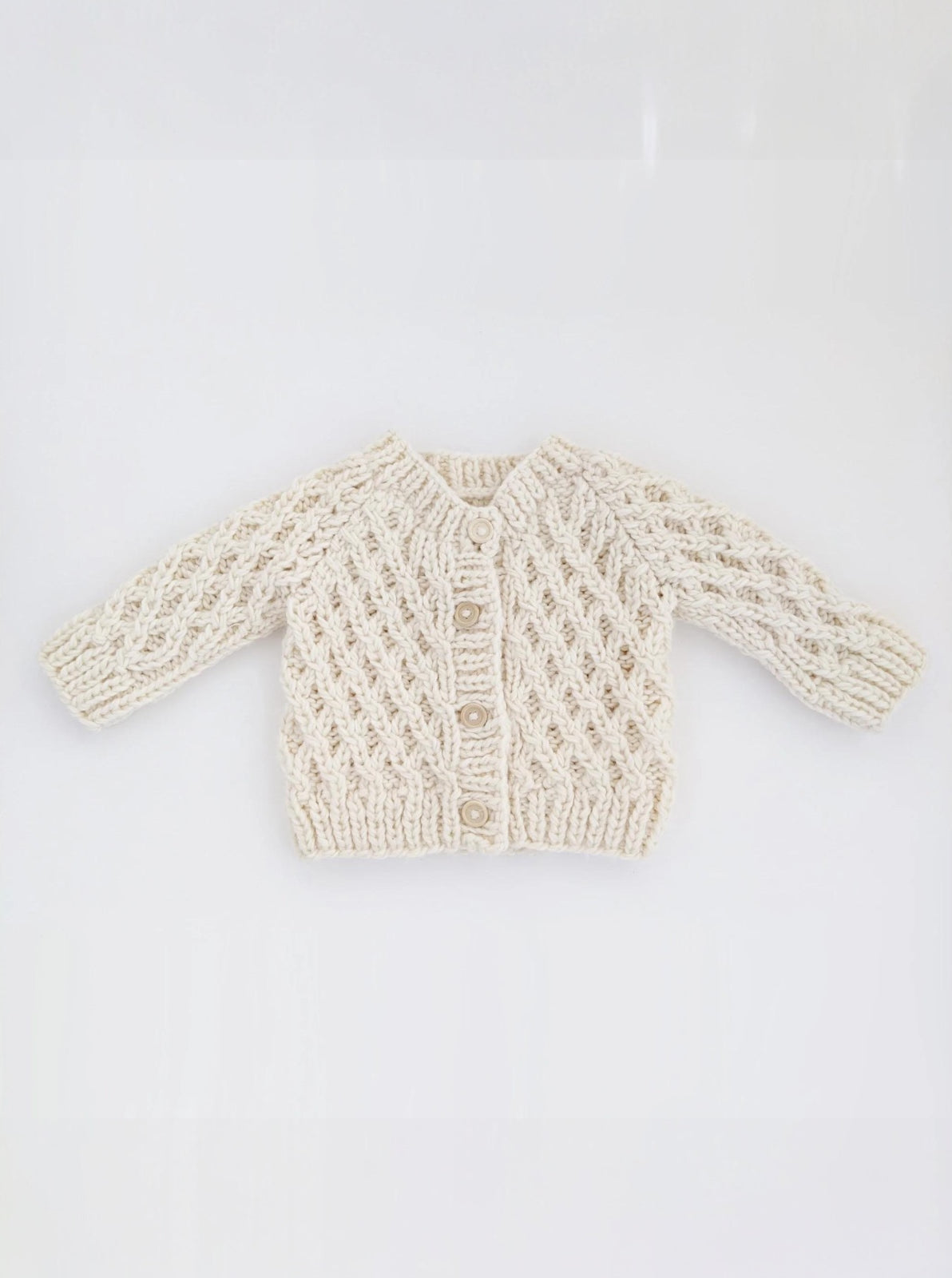 Cream-colored knitted baby cardigan with intricate patterns and three buttons at the front.