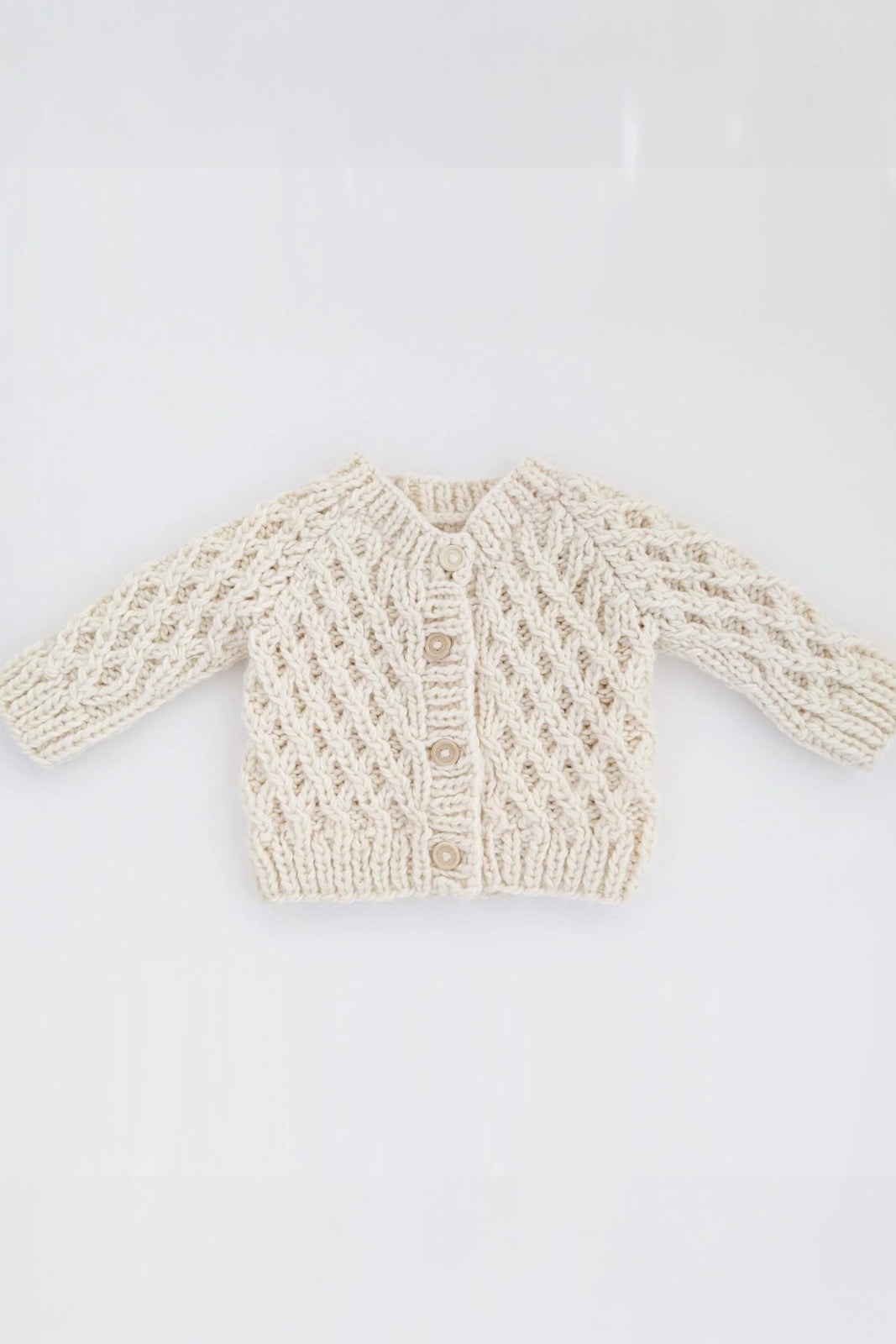 Cream-colored knitted baby cardigan with intricate patterns and three buttons at the front.