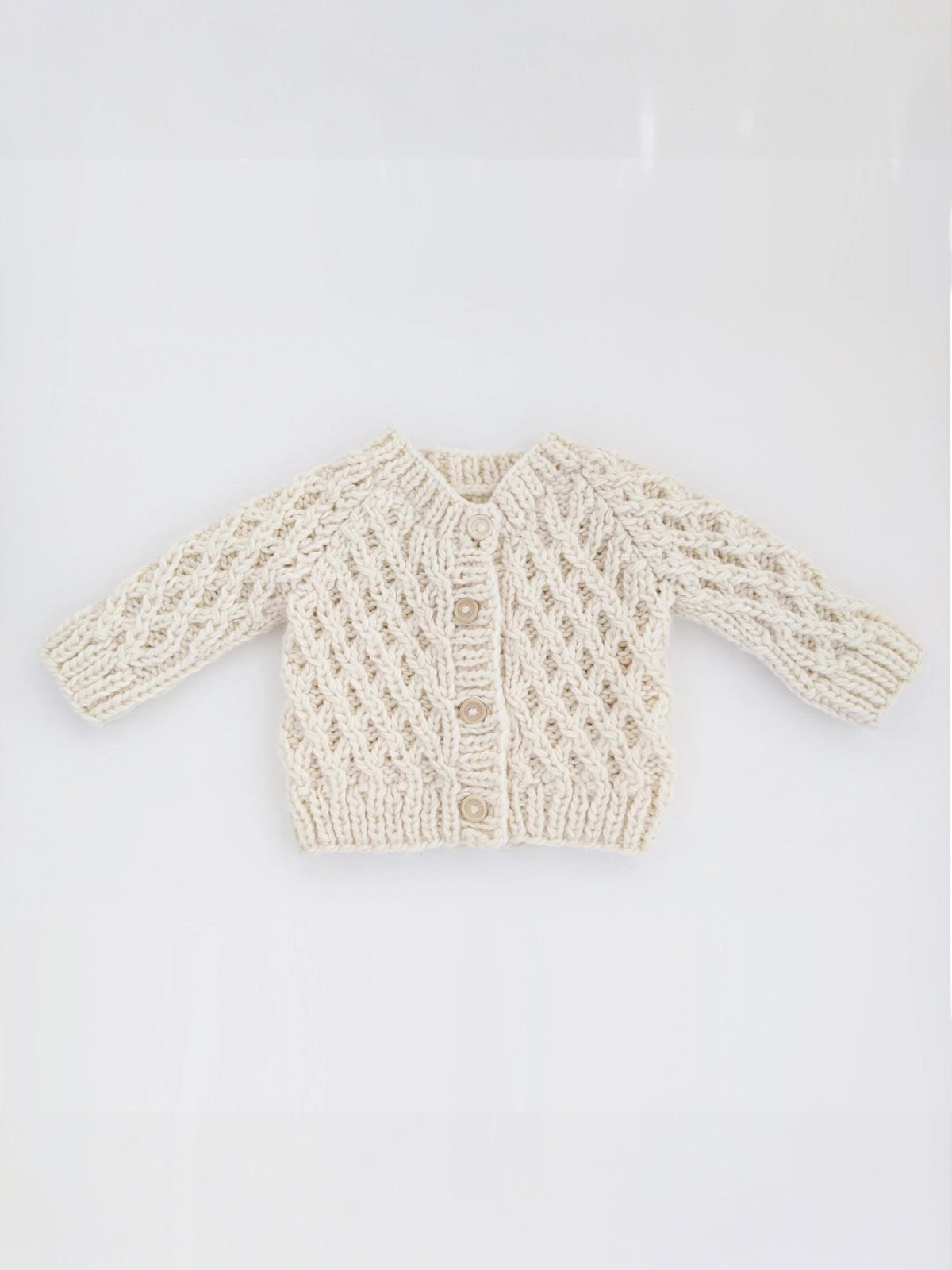 Cream-colored knitted baby cardigan with intricate patterns and three buttons at the front.