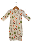 Patterned baby dress featuring bunnies, carrots, and green vegetables on a cream background, hanging on a wooden hanger.