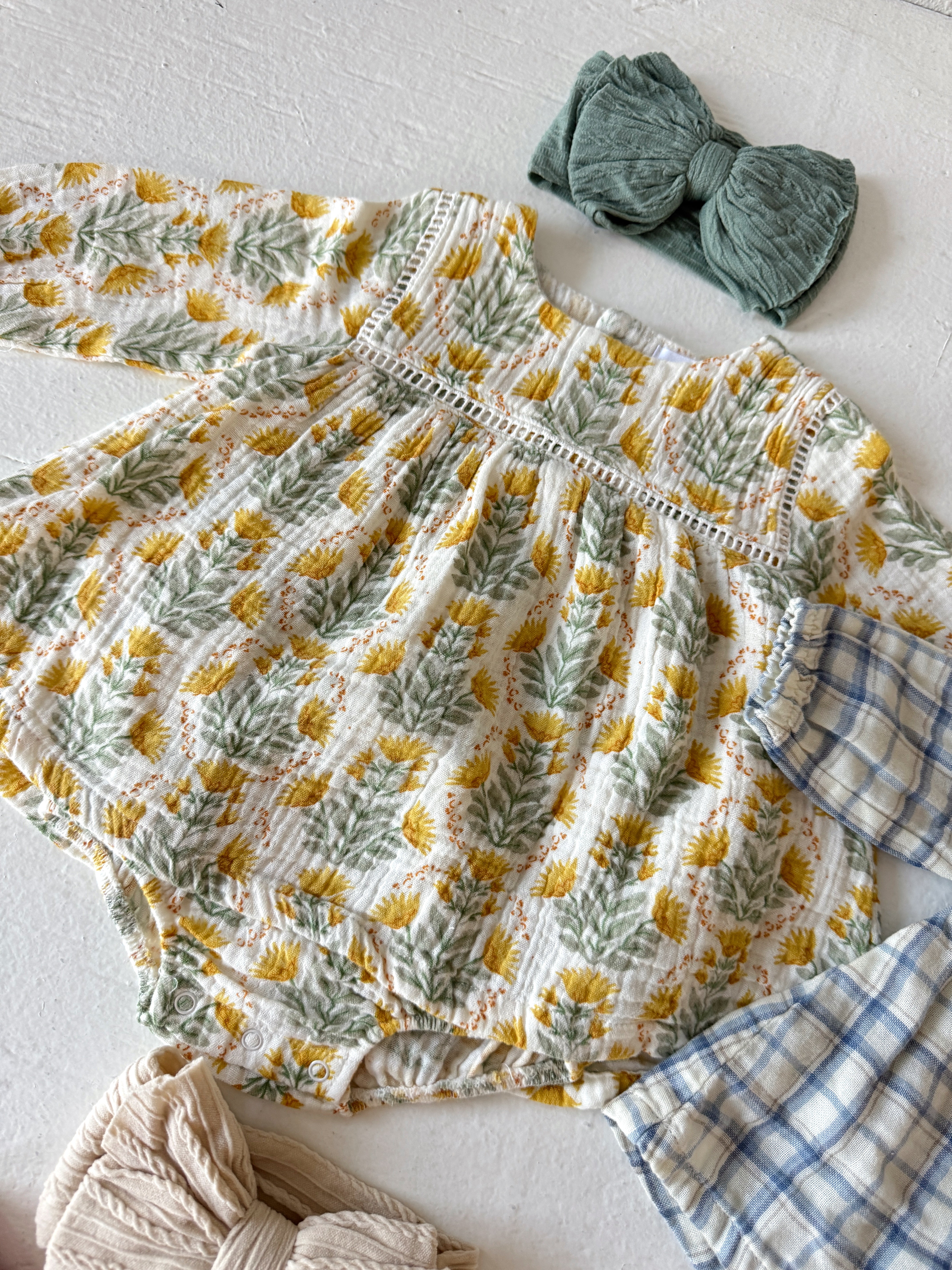 Floral baby outfit with long sleeves, green headband, and neutral accessories on a white surface.