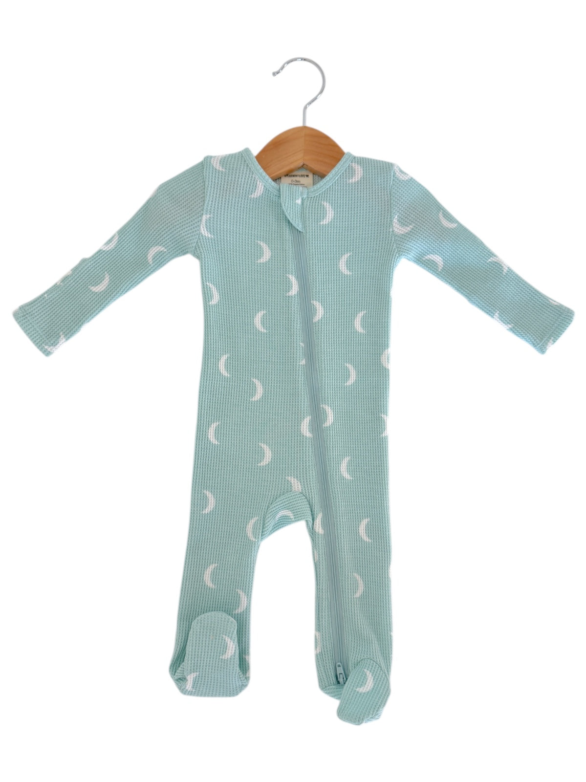 Light blue baby onesie with moon prints, featuring long sleeves and footed design, hanging on a wooden hanger.