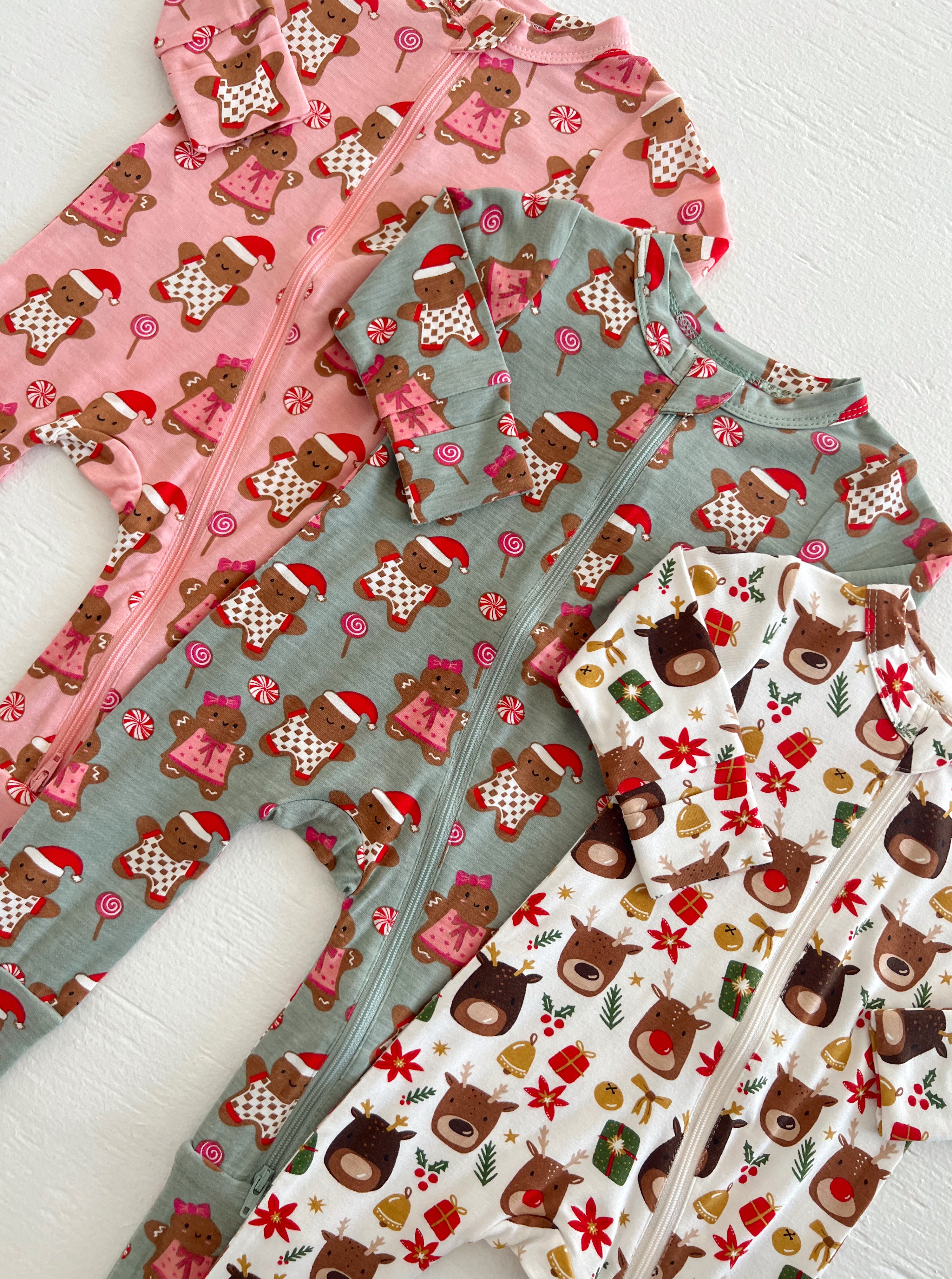 Three festive infant onesies featuring gingerbread and reindeer patterns in pink, green, and white colors.