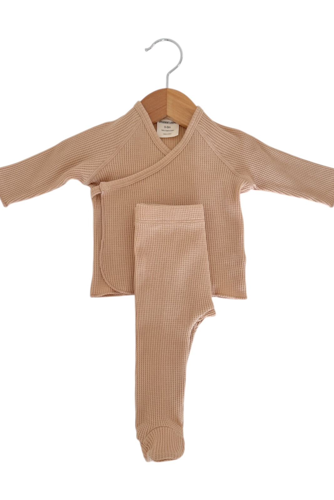 Light brown infant outfit hanging on a wooden hanger, featuring a wrap shirt and matching pants.