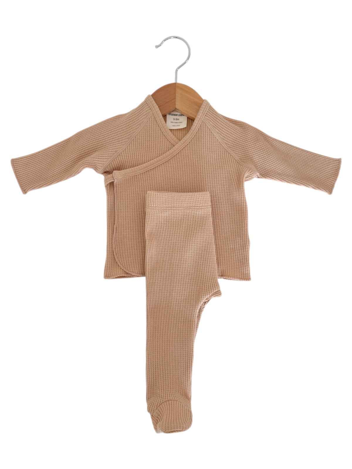 Light brown infant outfit hanging on a wooden hanger, featuring a wrap shirt and matching pants.