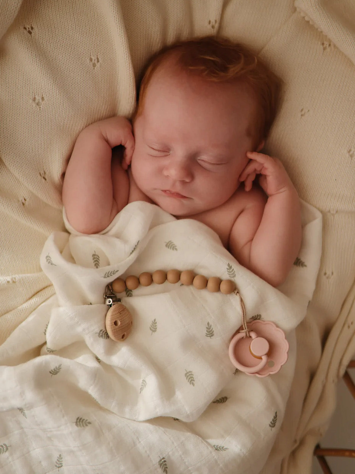 Sleeping newborn swaddled in a soft blanket with a teething toy nearby, peaceful and cozy.