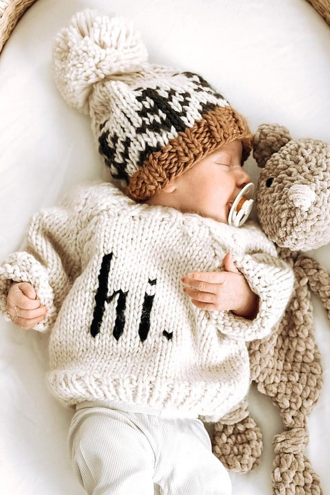 Baby sleeping in a cozy sweater and hat, cuddling a plush toy, with a peaceful expression.