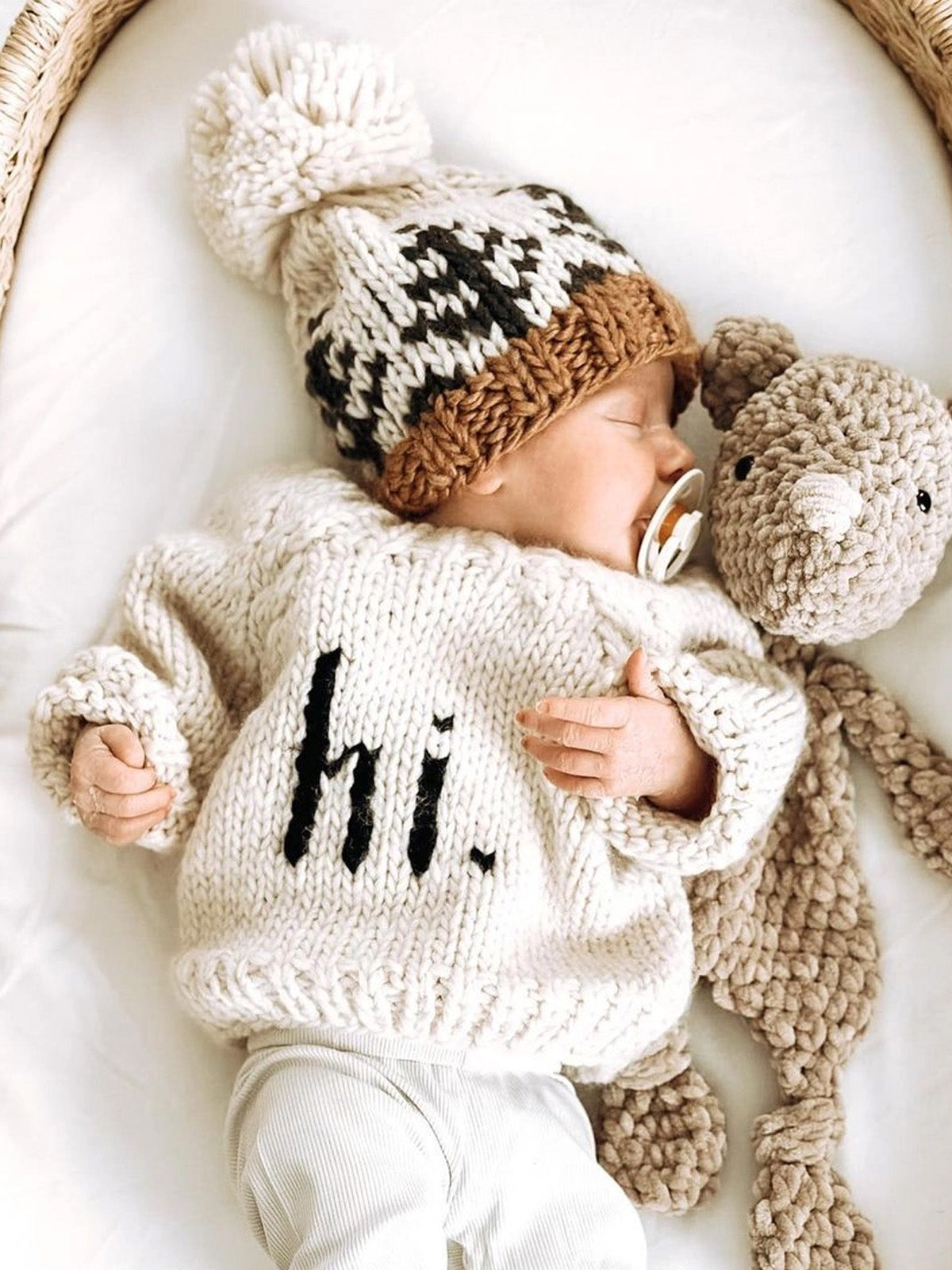Baby sleeping in a cozy sweater and hat, cuddling a plush toy, with a peaceful expression.