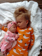 Two sleeping children on a cozy blanket, one in orange ghost-patterned pajamas, the other in pink.