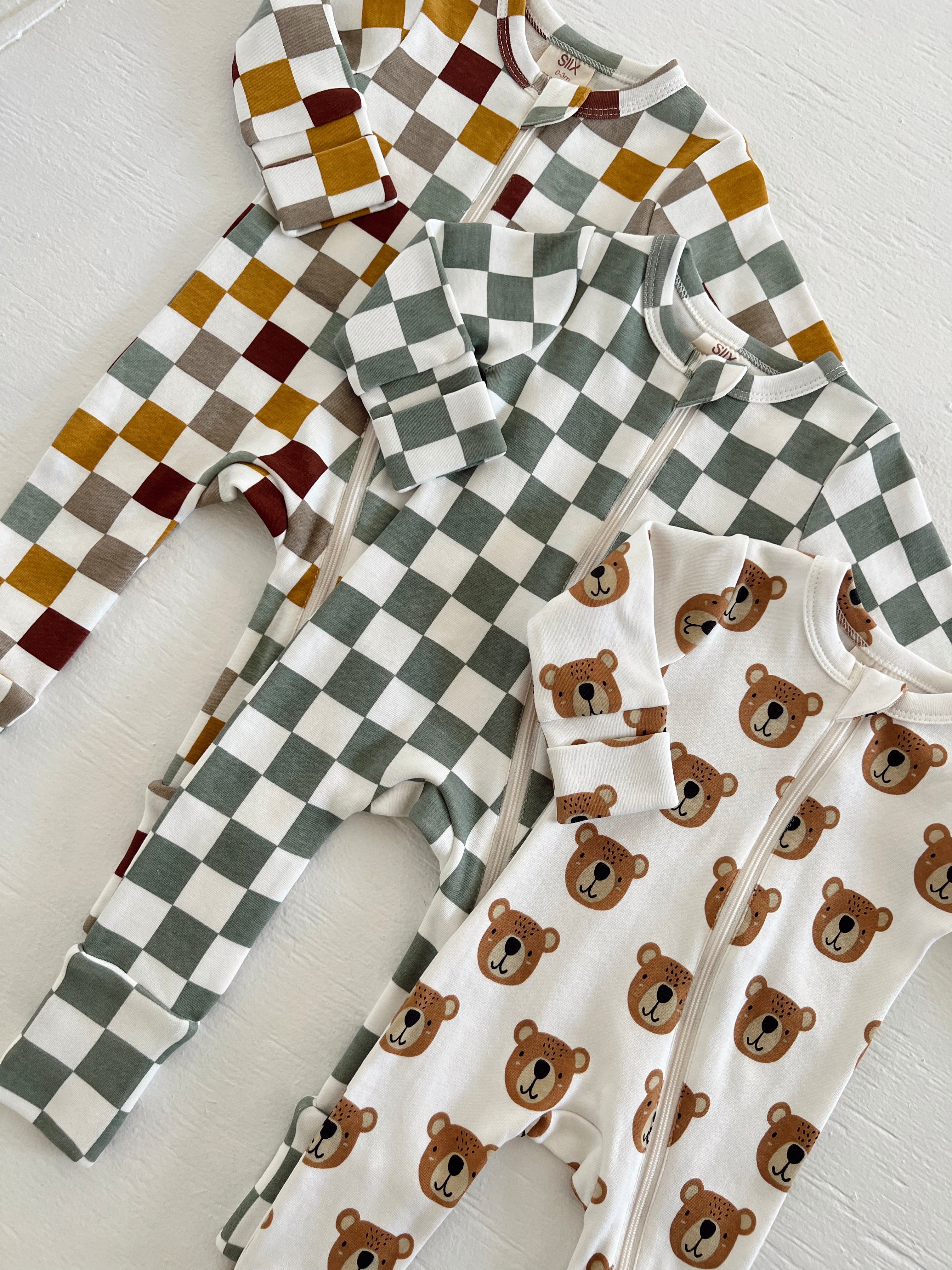 Three baby onesies: two with checkered patterns and one with bear faces on a white background.