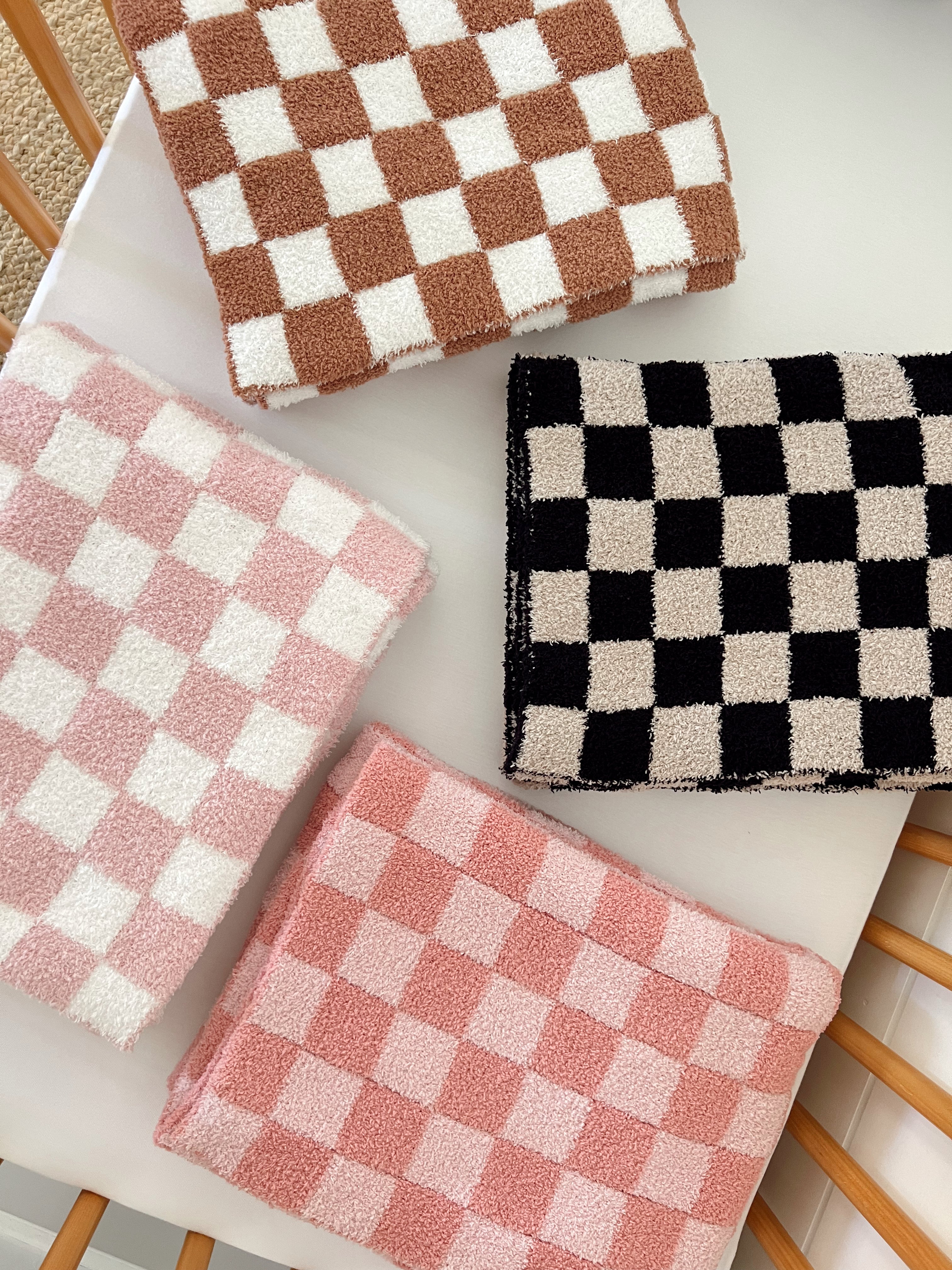 Four checkered towels in pink, brown, and black on a neutral surface, showcasing a soft texture and vibrant colors.