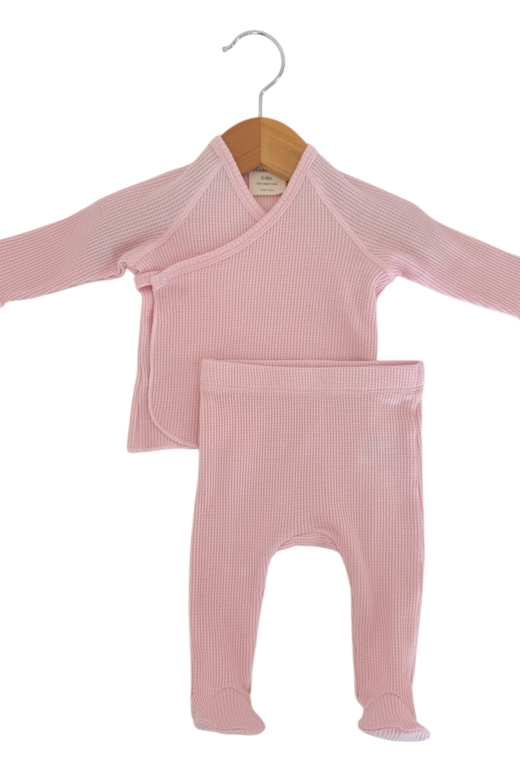 Pink infant outfit consisting of a long-sleeve wrap top and matching pants hanging on a wooden hanger.