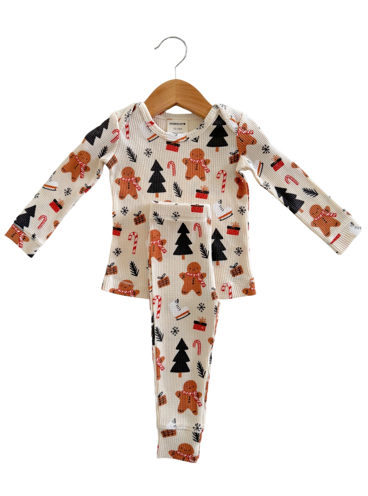 Child's holiday pajamas featuring gingerbread men, candy canes, and Christmas trees on a cream background.