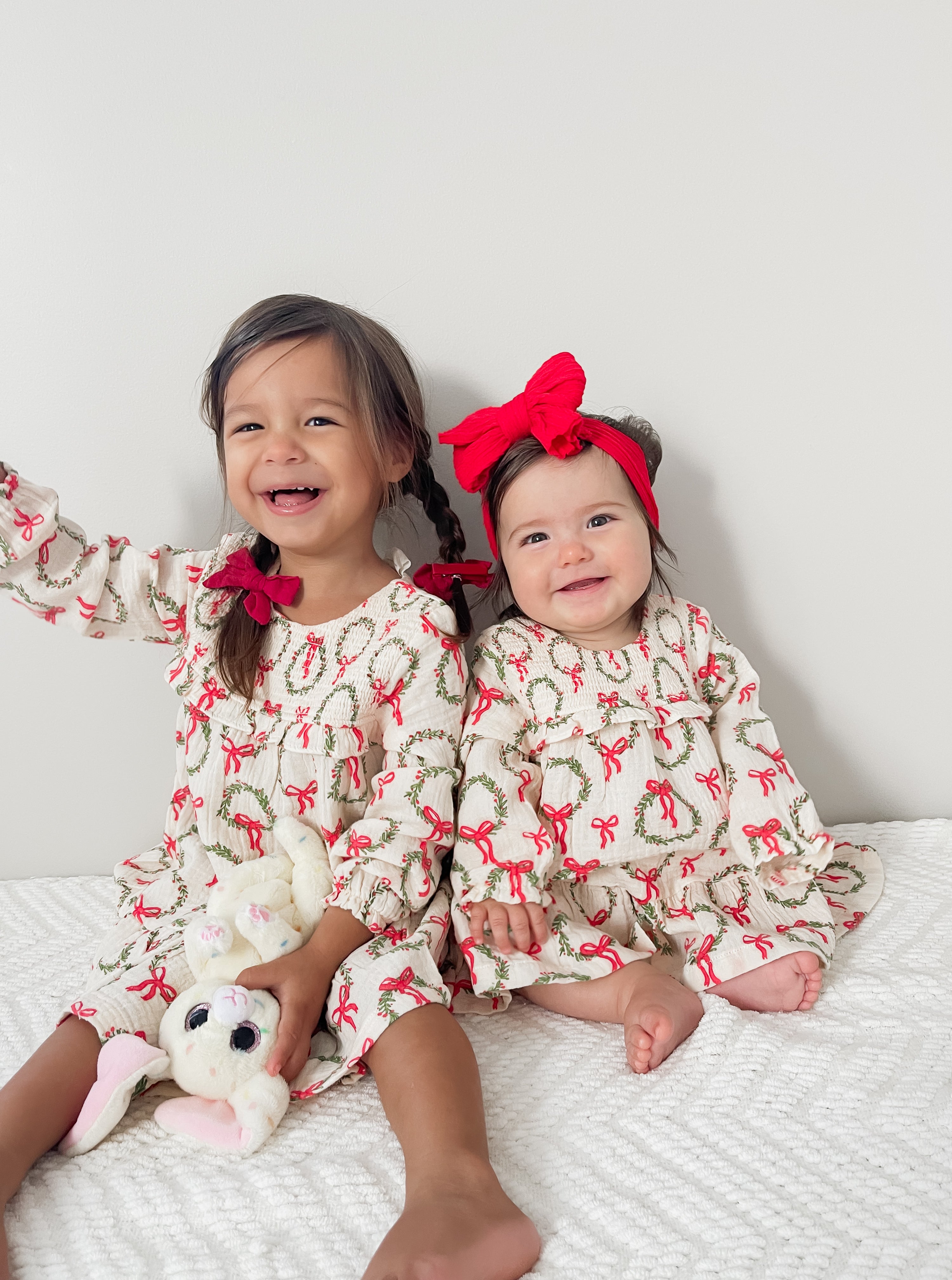 Two smiling young girls in matching holiday dresses, one holding a bunny toy, against a white background.