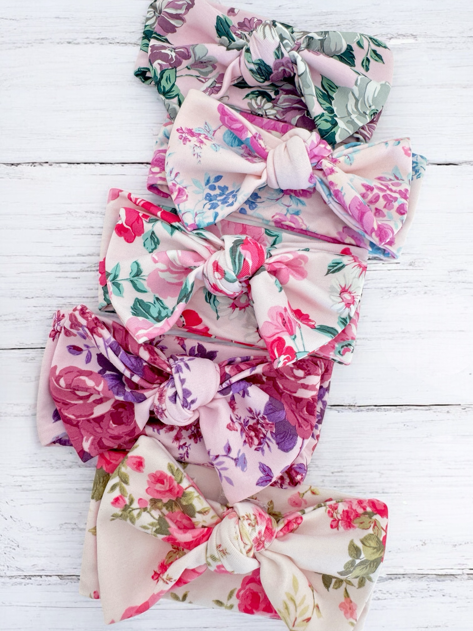 Five floral-patterned fabric bows arranged neatly on a wooden background.