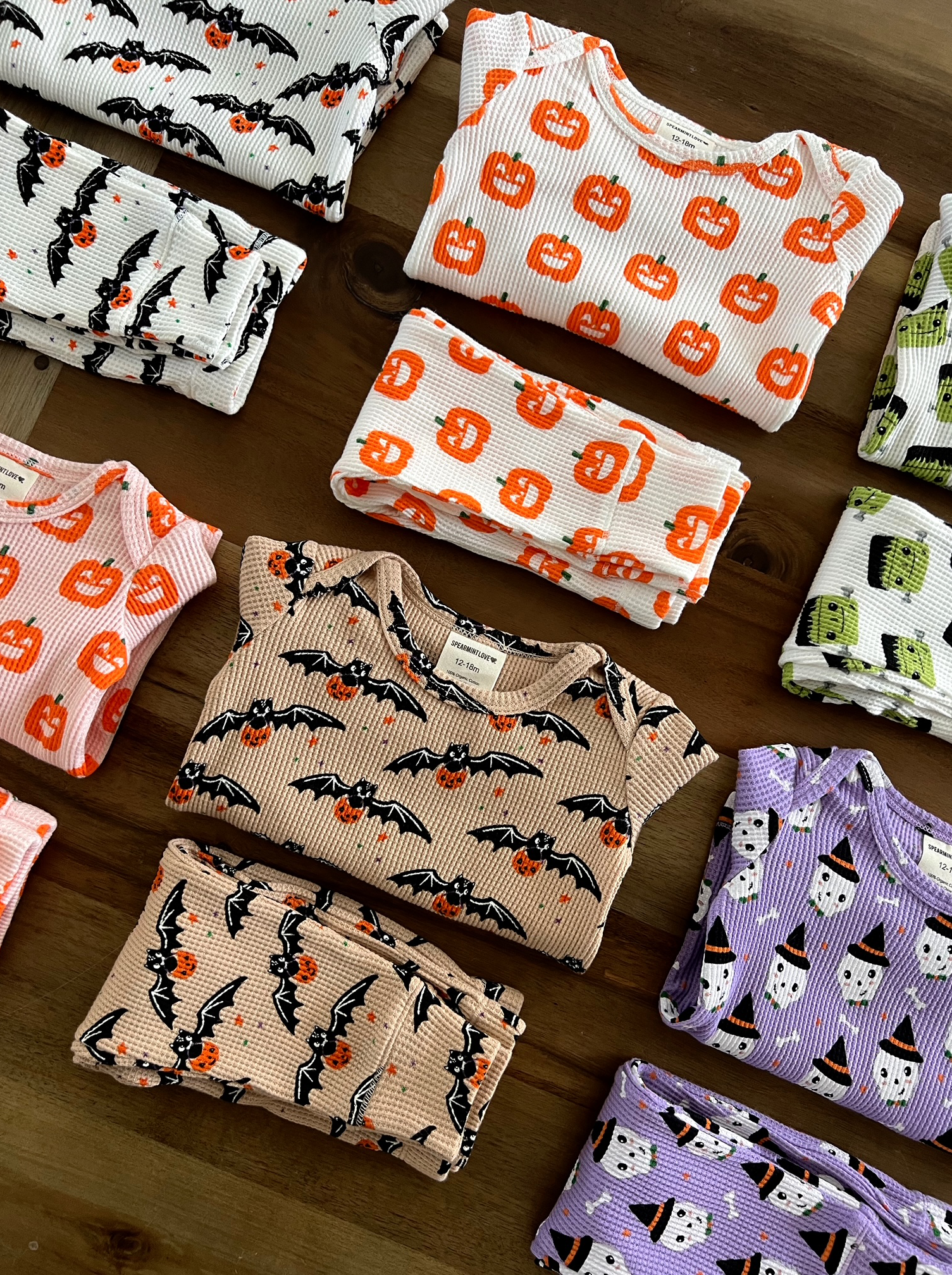 Colorful Halloween-themed children’s pajamas with bats, pumpkins, and ghosts arranged neatly on a wooden surface.
