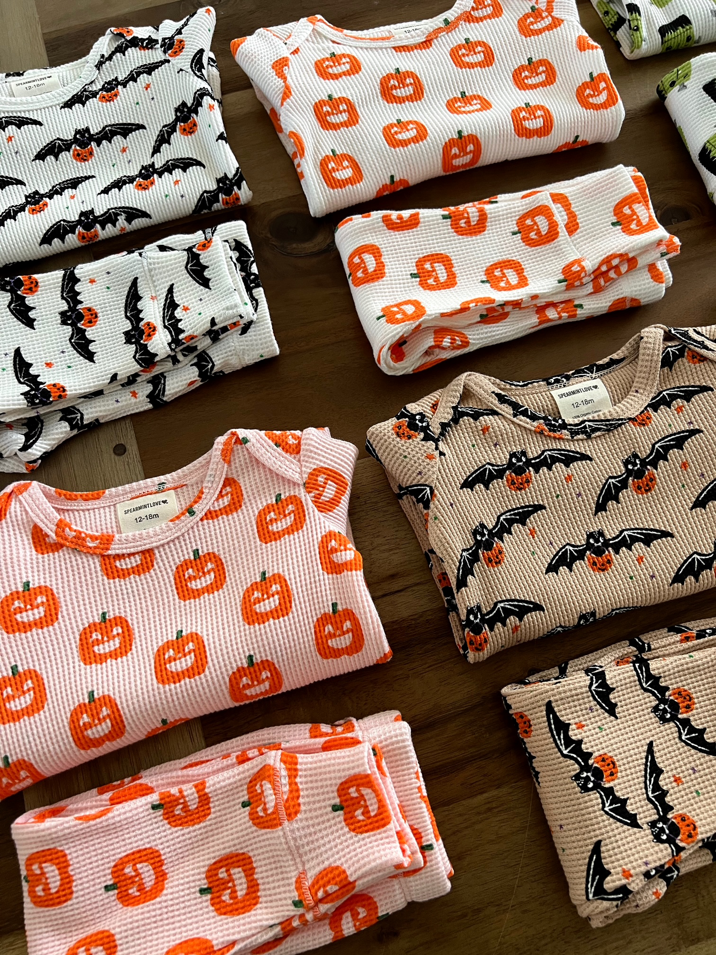 Assorted Halloween-themed pajamas featuring bats and pumpkins, neatly folded on a wooden surface.
