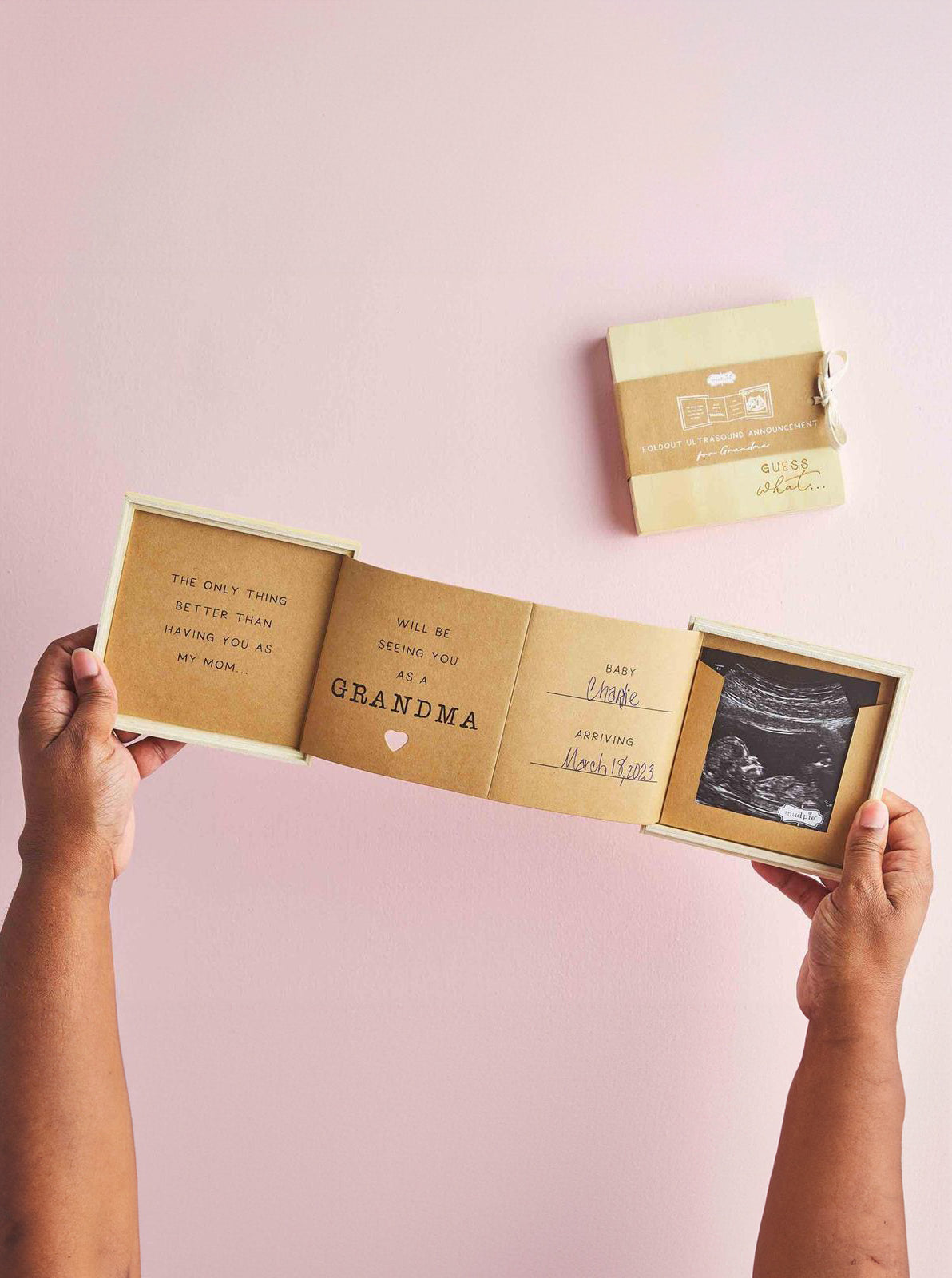 A person holds an announcement card revealing a baby coming soon, with an ultrasound photo and heartfelt messages.