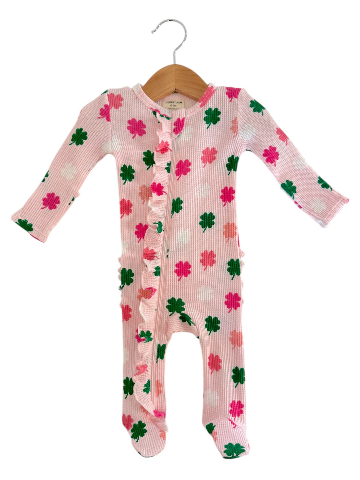 Pink children's onesie with floral patterns and ruffles, hanging on a wooden hanger against a white background.