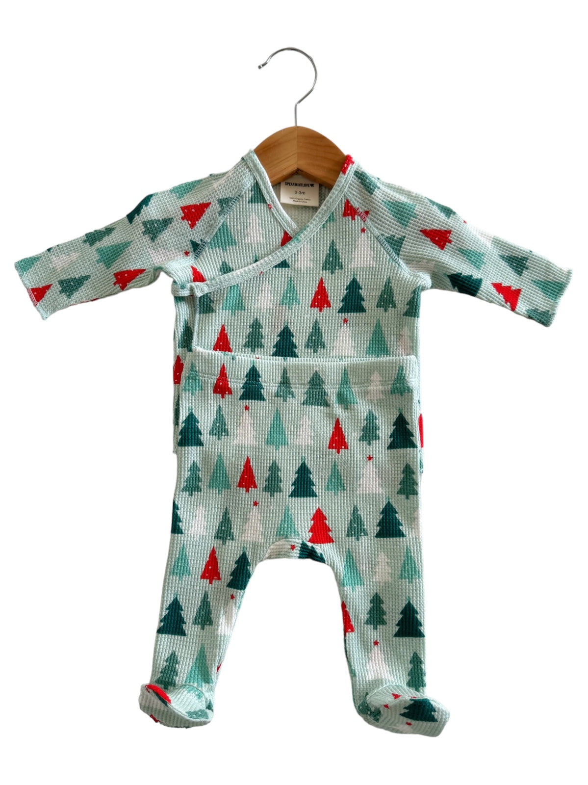Mint green children's outfit with red and green Christmas tree patterns, hanging on a wooden hanger.