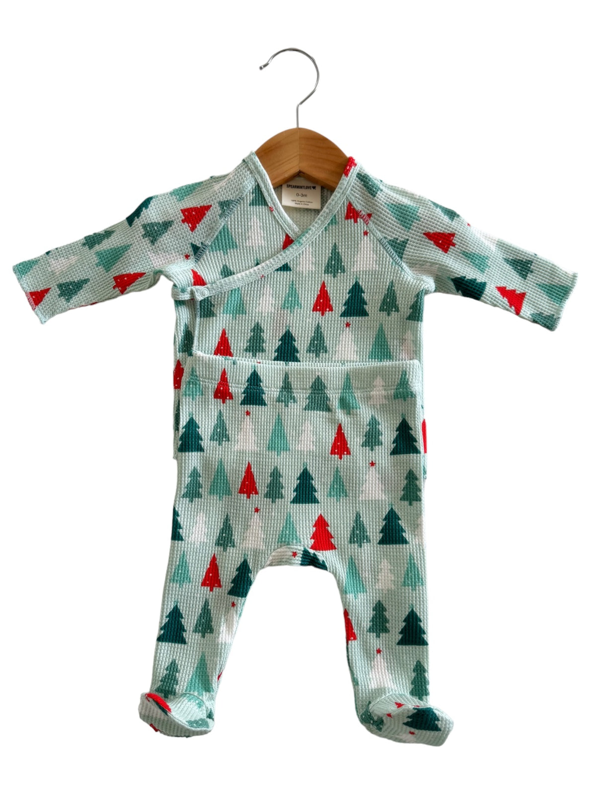Mint green children's outfit with red and green Christmas tree patterns, hanging on a wooden hanger.