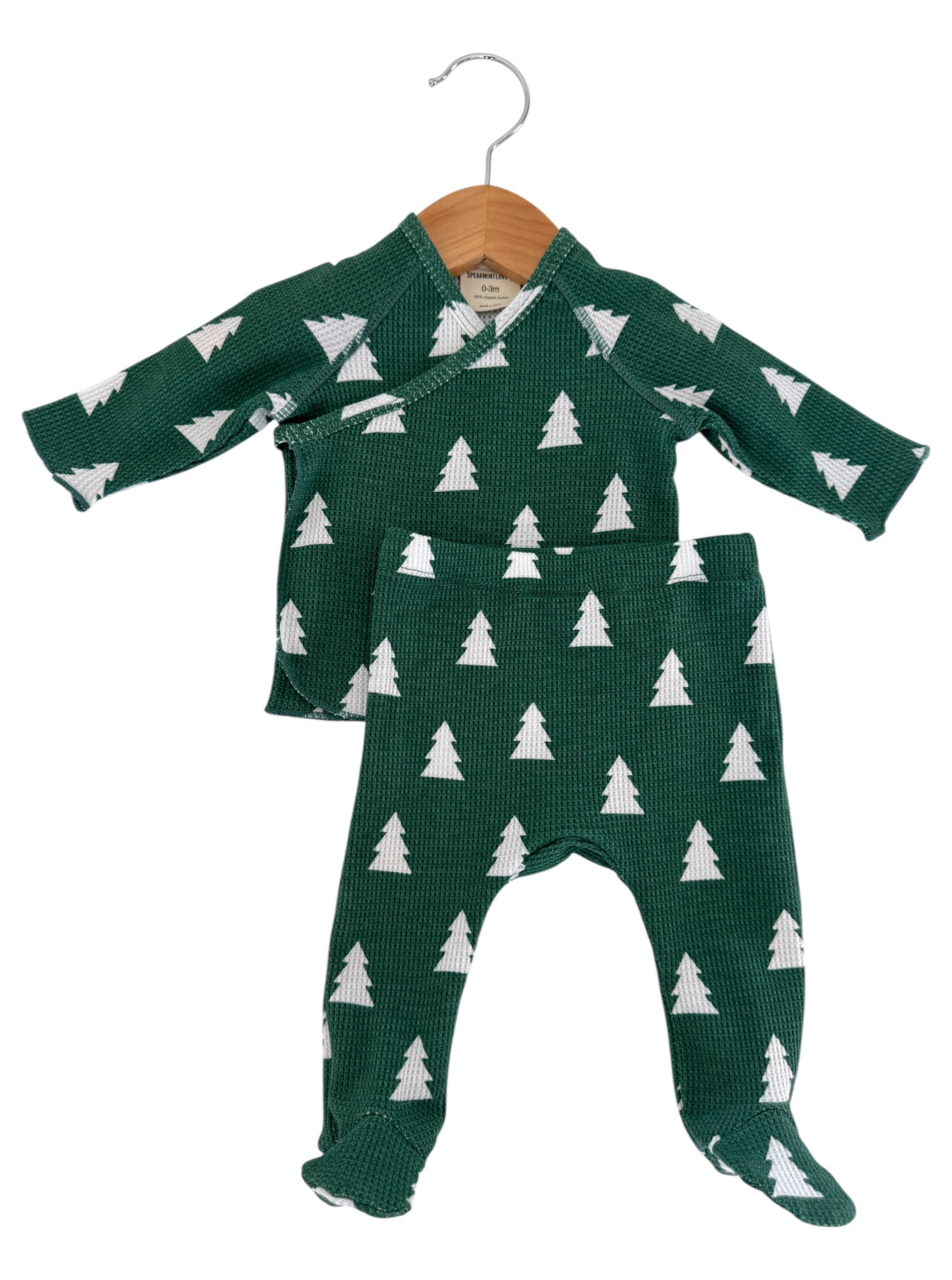 Green baby outfit with white tree patterns, including a top and pants, displayed on a wooden hanger.