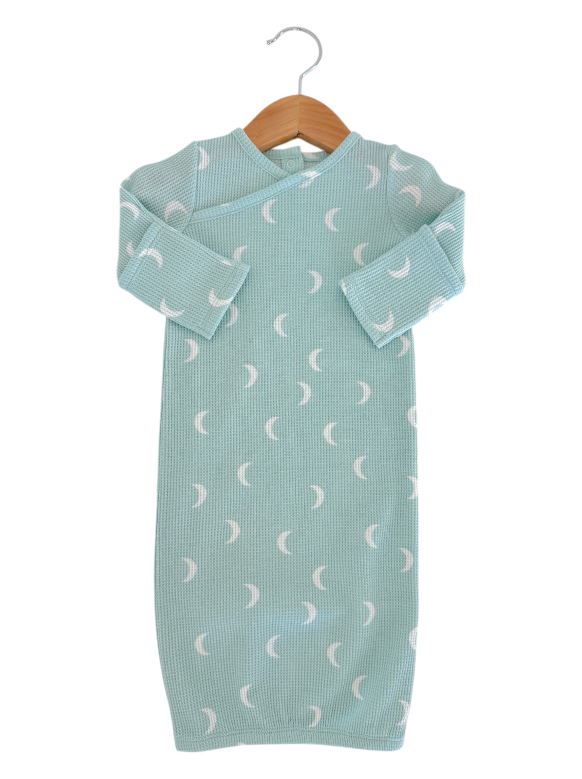 Light blue baby gown with moon patterns, hanging on a wooden hanger against a white background.