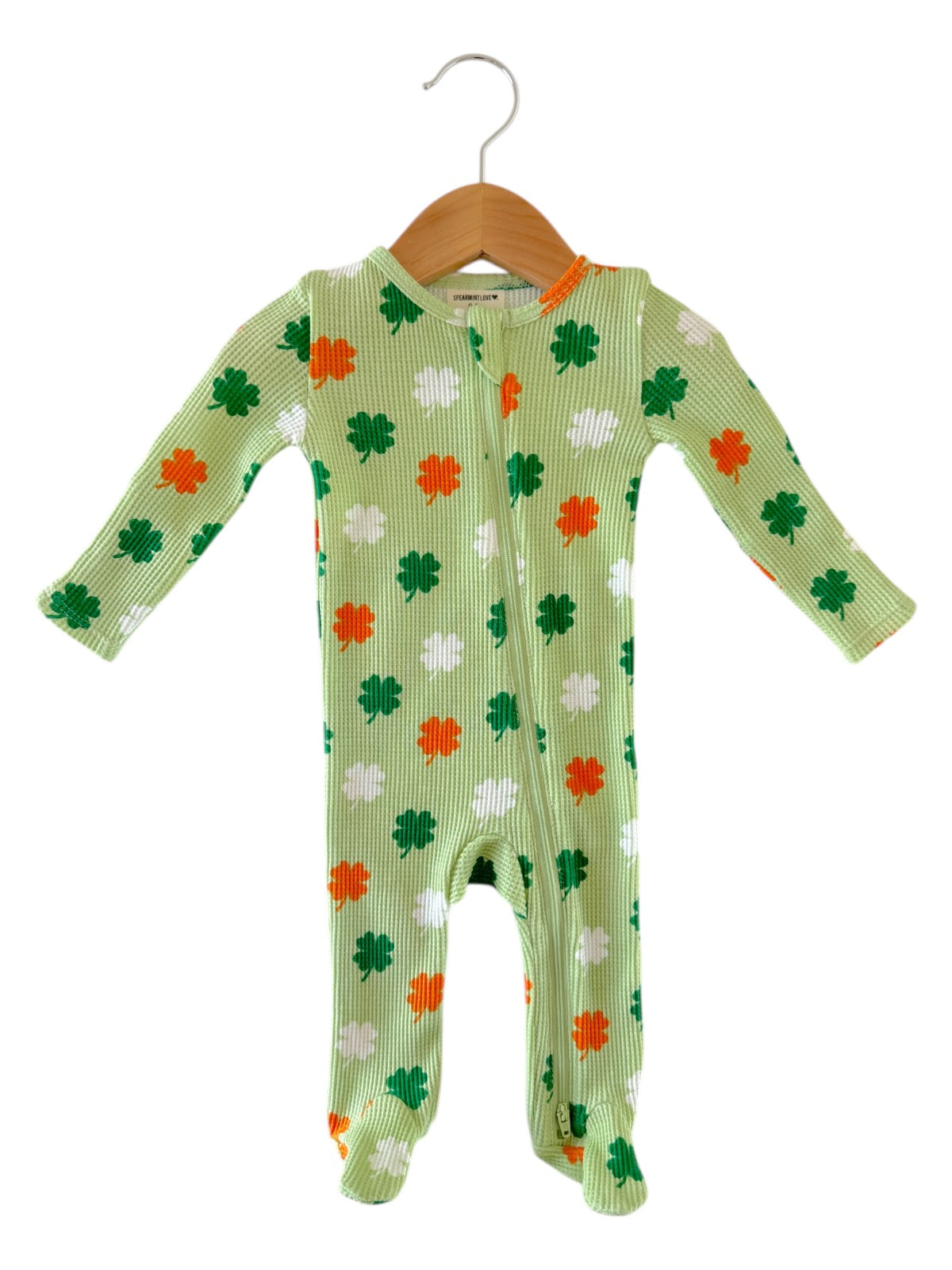 Green baby onesie with white, orange, and green clover patterns, hanging on a wooden hanger.