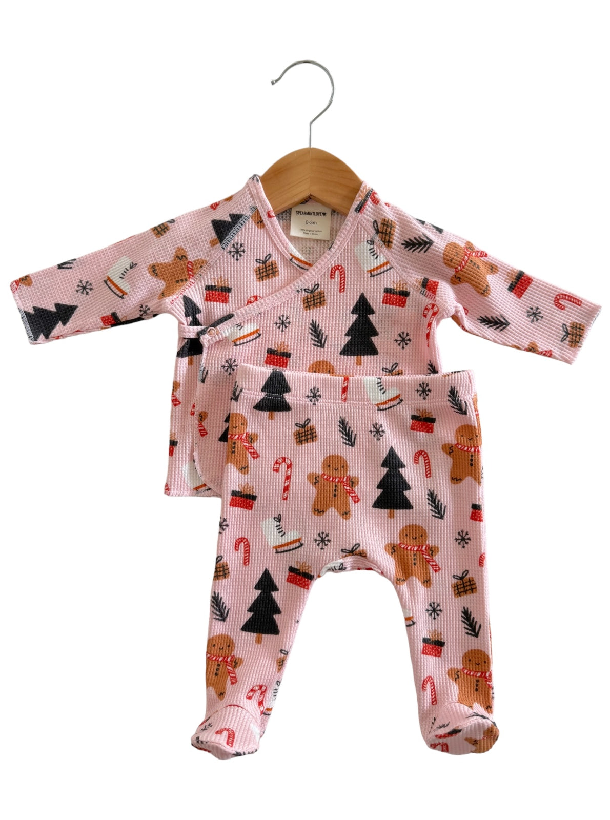 Pink baby outfit featuring gingerbread men, candy canes, and Christmas trees, hanging on a wooden hanger.
