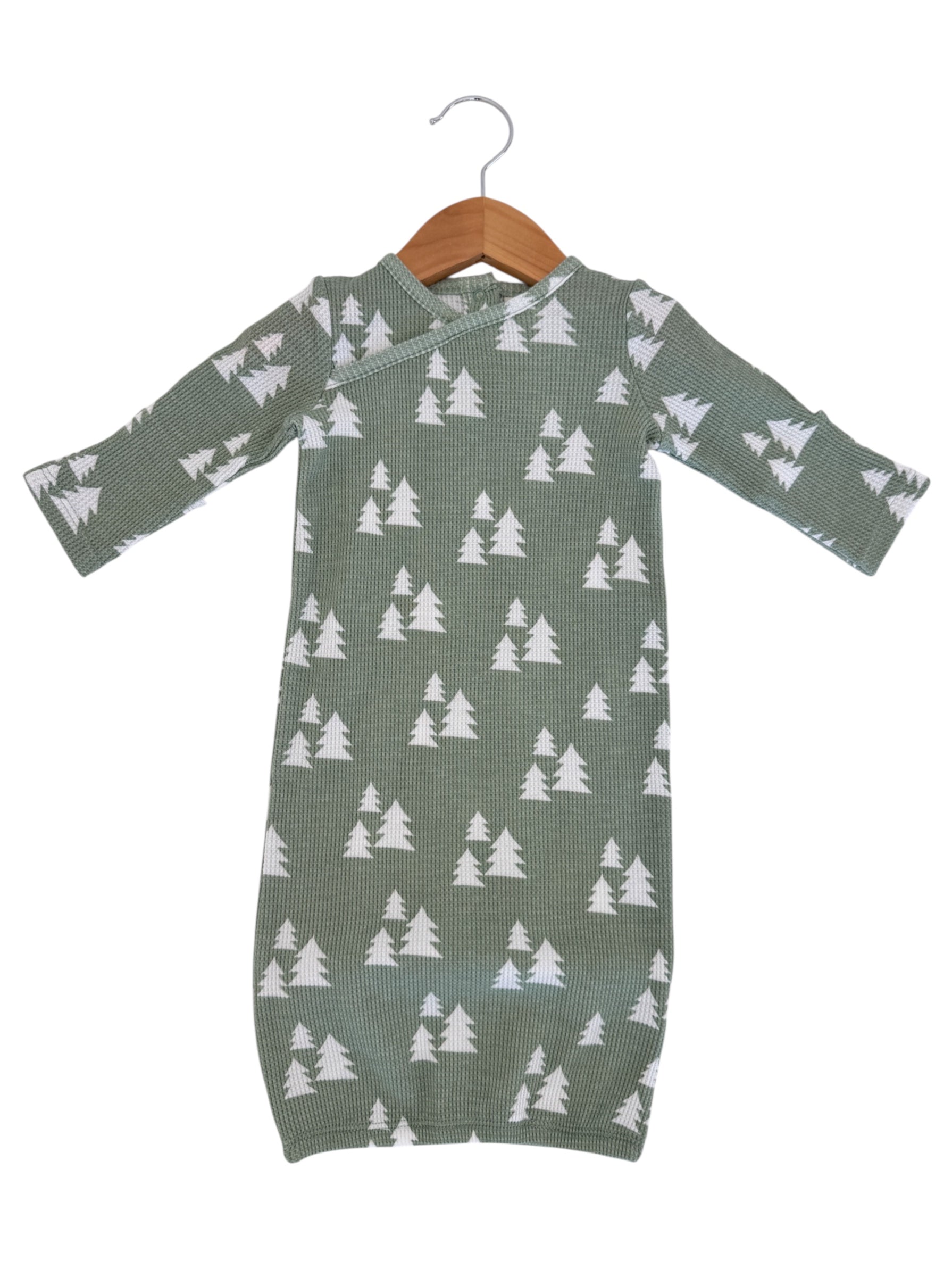 Green infant dress with white tree pattern, hanging on a wooden hanger against a white background.