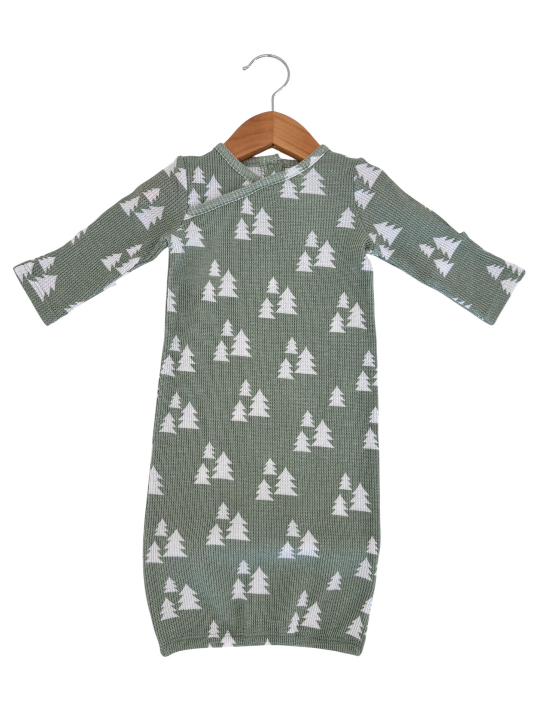 Green infant dress with white tree pattern, hanging on a wooden hanger against a white background.