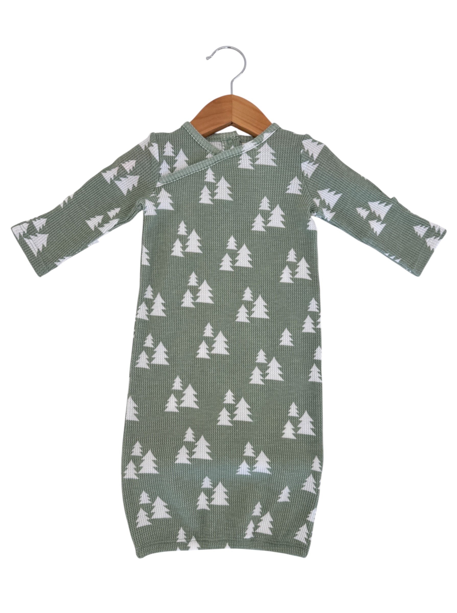 Green infant dress with white tree pattern, hanging on a wooden hanger against a white background.