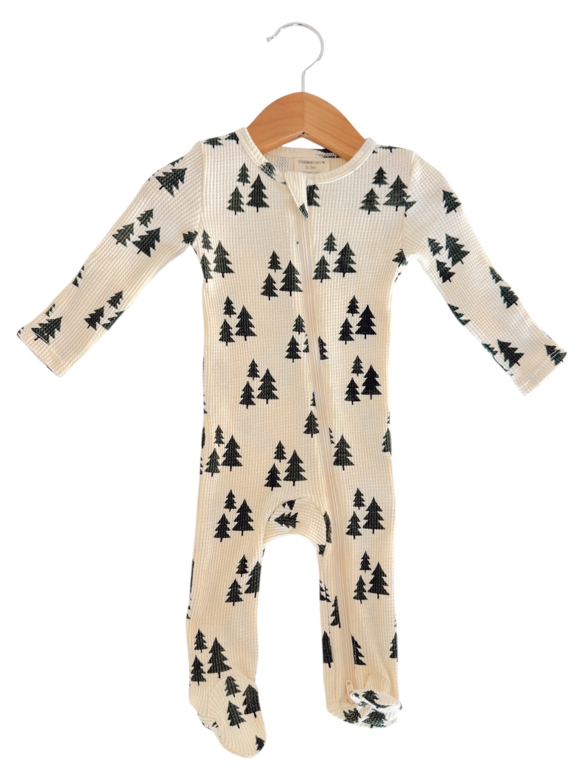 Light-colored baby onesie with tree patterns, hanging on a wooden hanger against a white background.