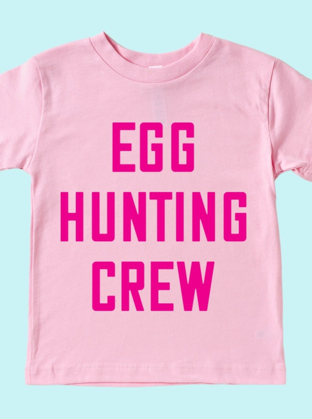 Pink t-shirt with bold text reading "EGG HUNTING CREW" on a light blue background.