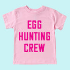Pink t-shirt with bold text reading "EGG HUNTING CREW" on a light blue background.