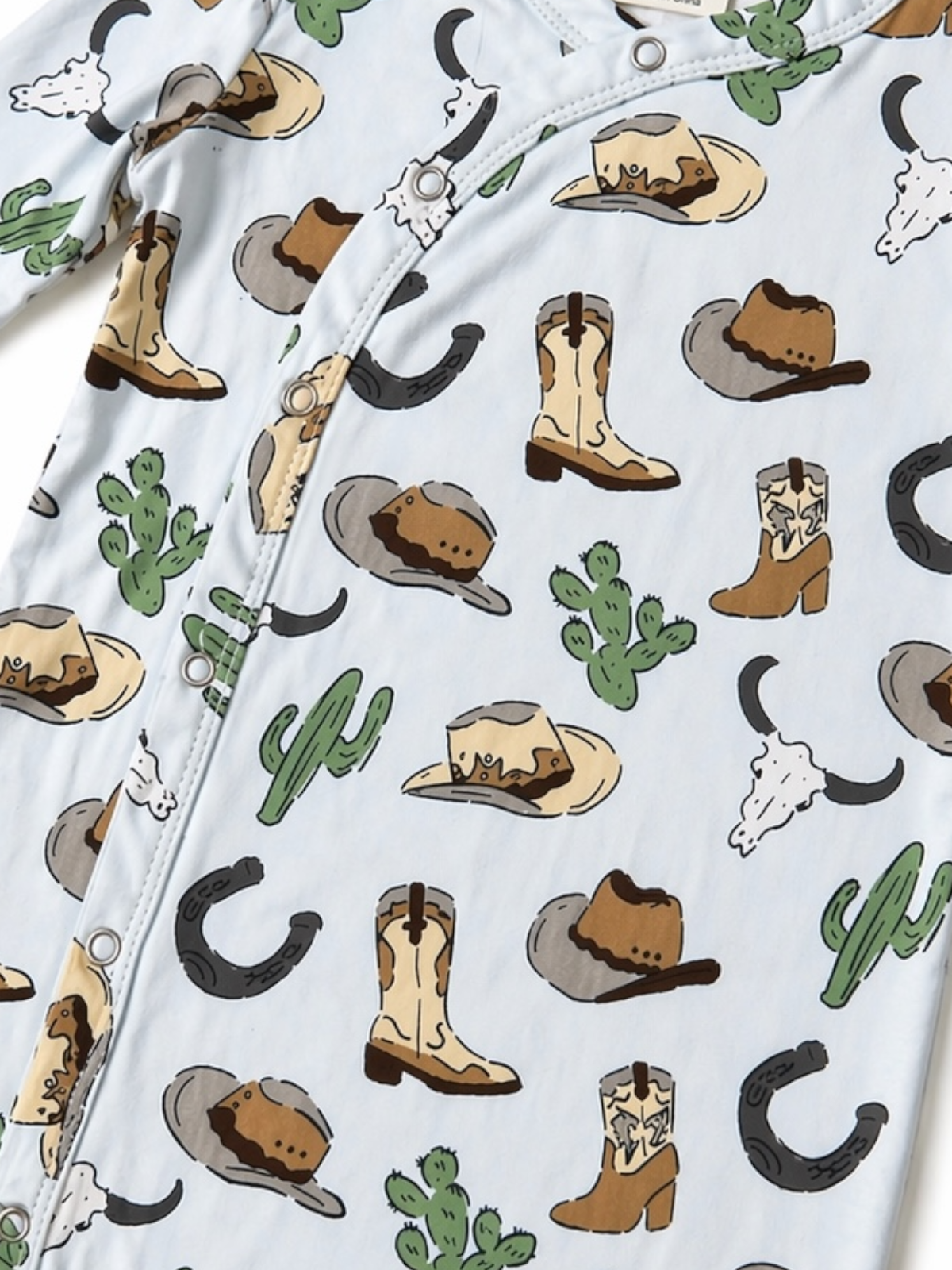 A light blue onesie with a western theme, featuring hats, boots, cacti, and cow skulls in playful patterns.