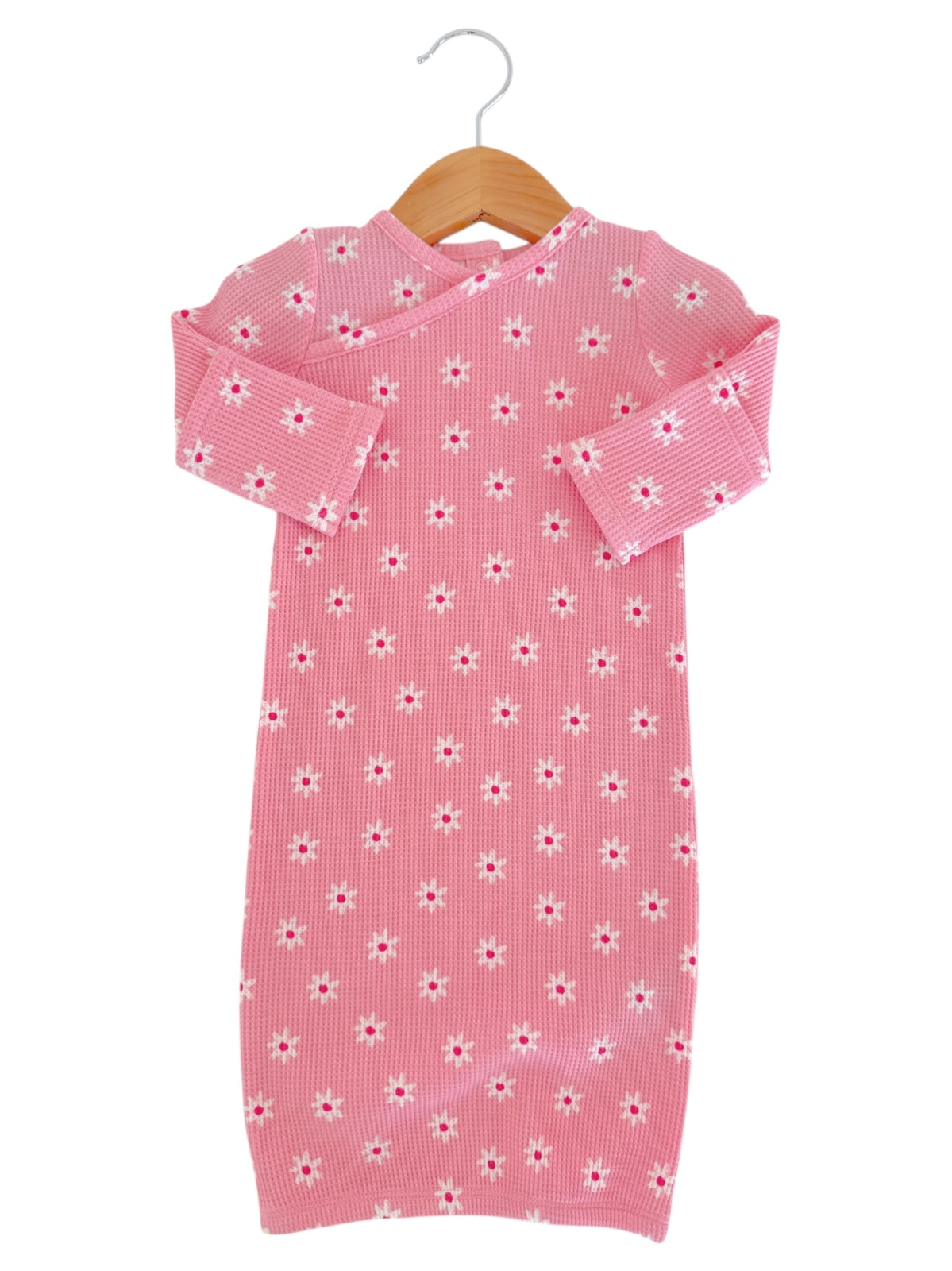 Pink dress with white floral patterns hanging on a wooden hanger against a white background.