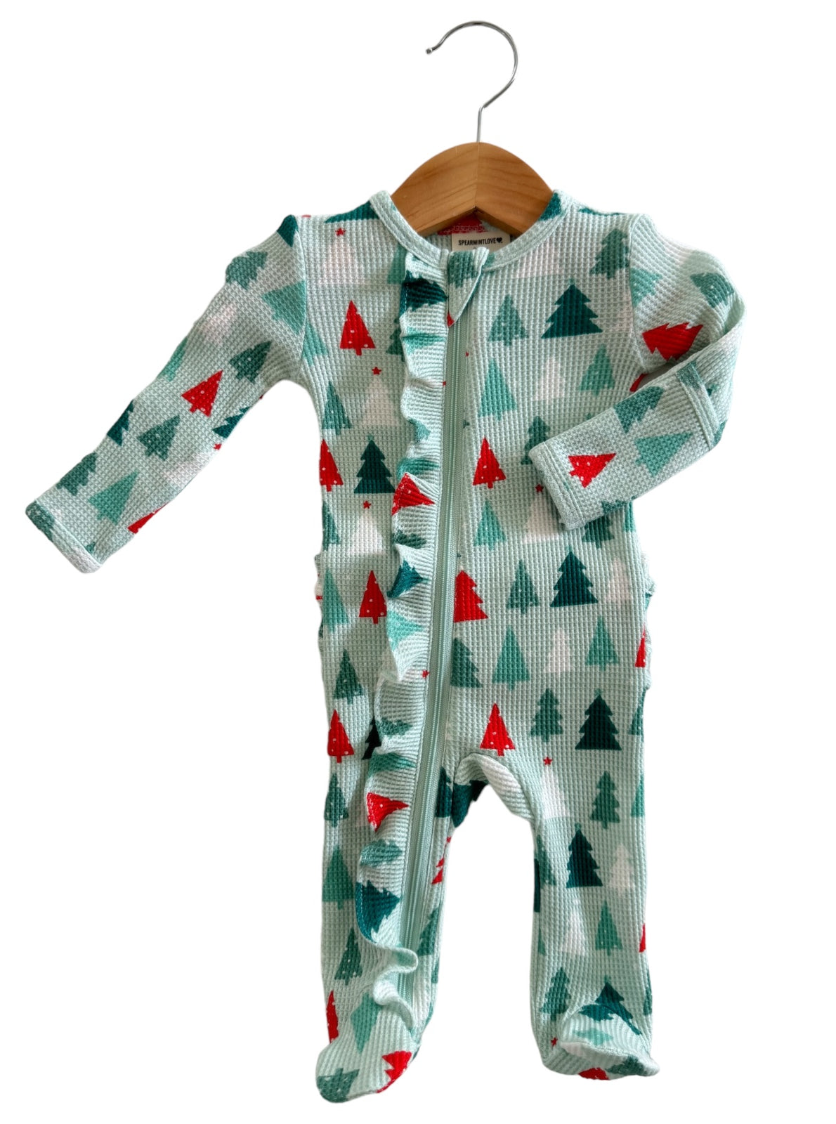 Green holiday onesie with red and teal trees, featuring a front zipper and ruffle detailing, hanging on a wooden hanger.